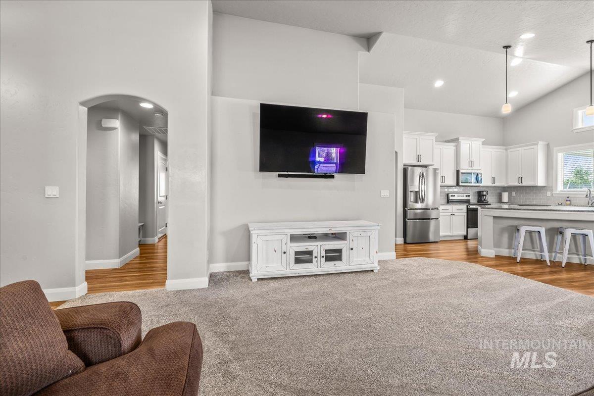 Living room featuring lofted ceiling, light colored carpet, arched walkways, a textured ceiling, and recessed lighting