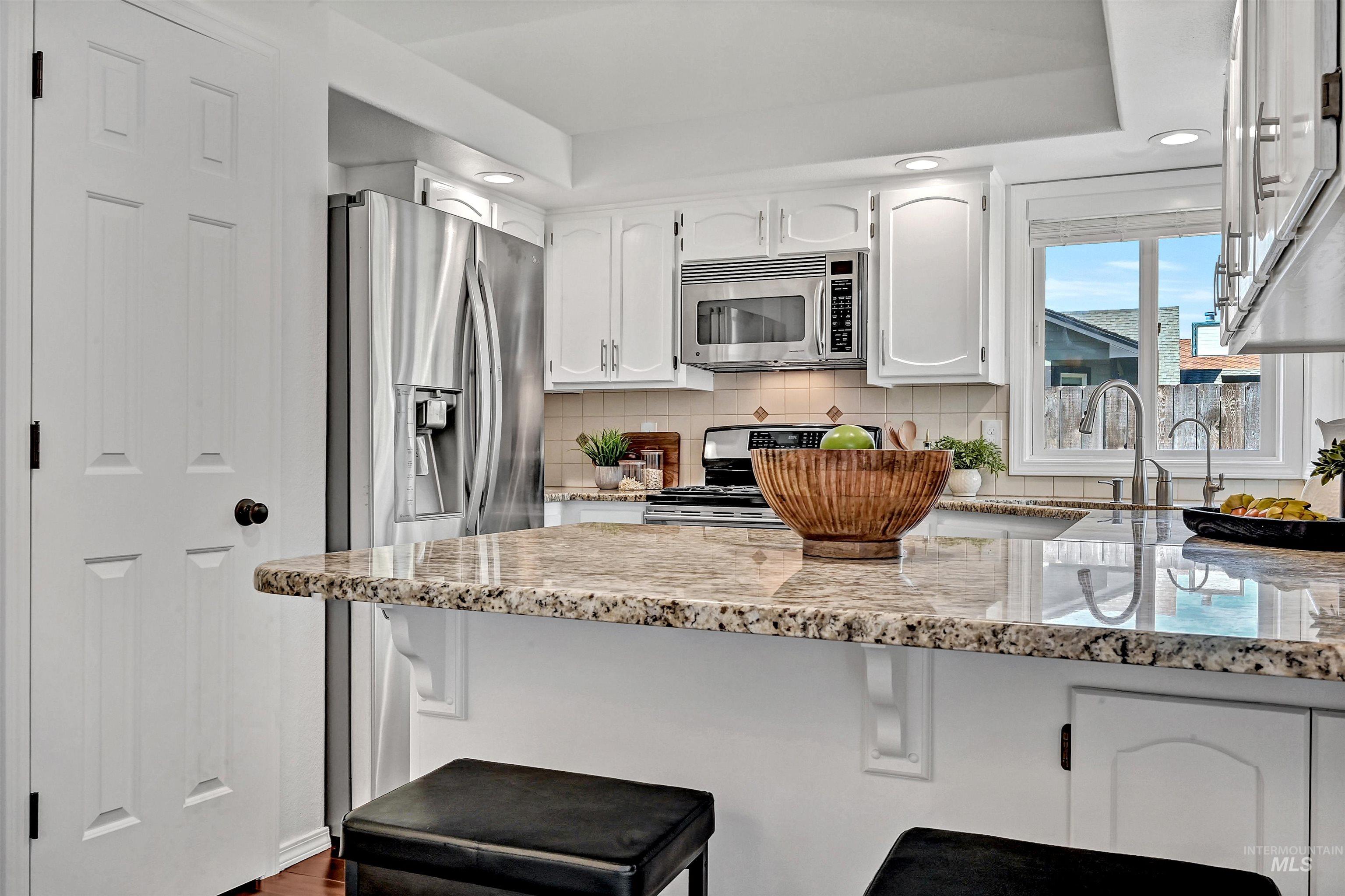 Kitchen with light stone counters, white cabinetry, backsplash, a kitchen bar, and recessed lighting