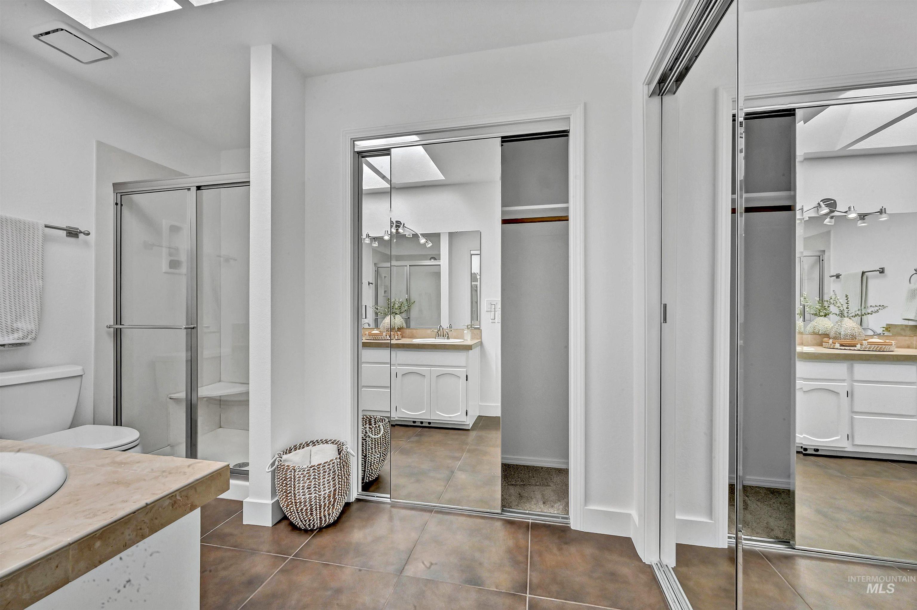 Bathroom featuring two vanities, a shower stall, dark tile patterned floors, and a skylight