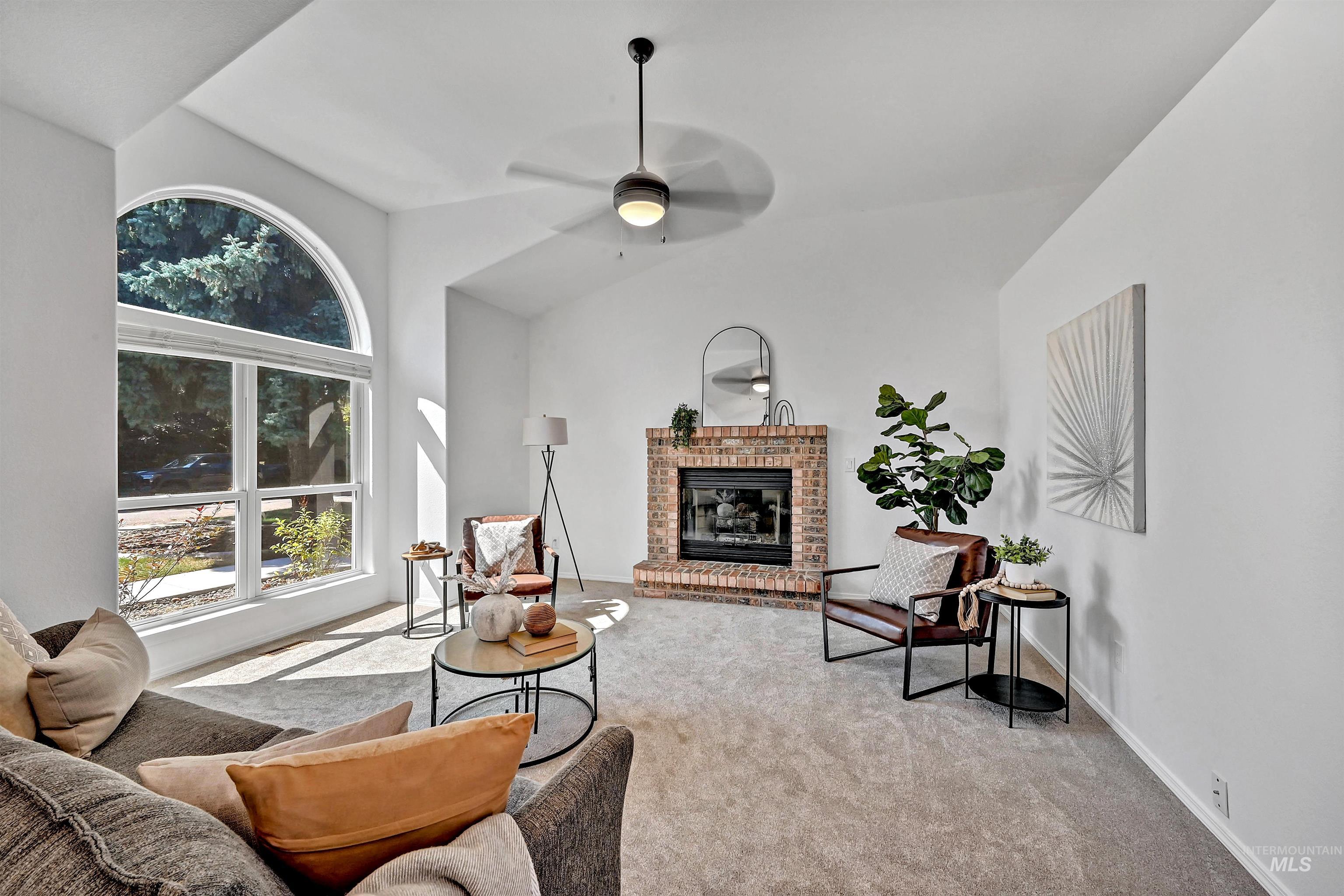 Living area featuring light colored carpet, ceiling fan, a brick fireplace, and lofted ceiling