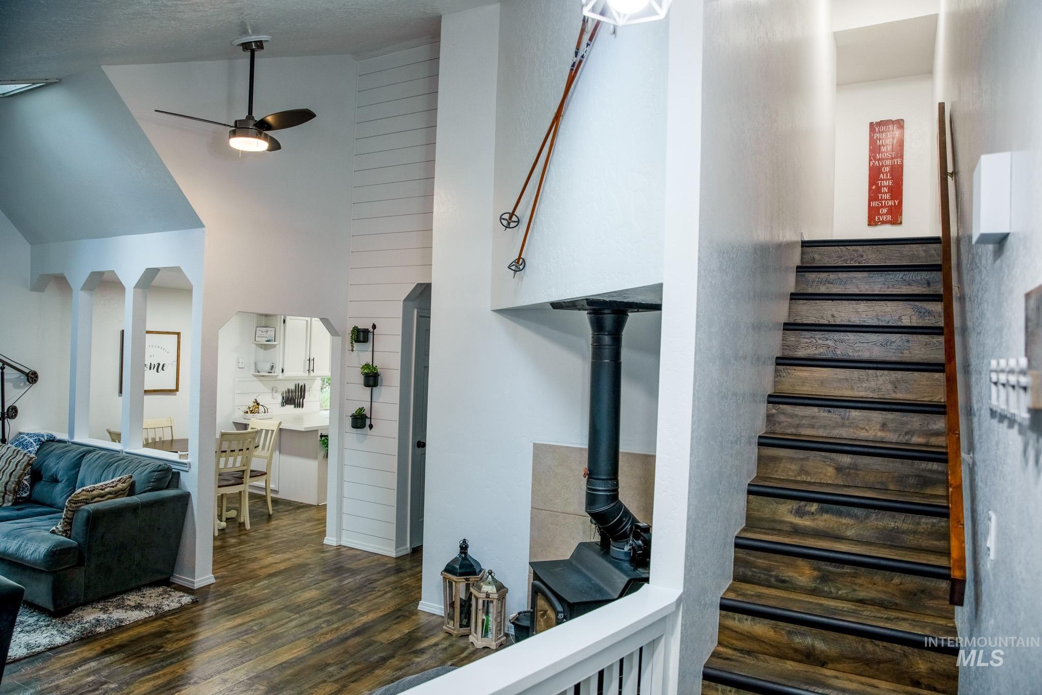 Stairs with wood finished floors, ceiling fan, arched walkways, and high vaulted ceiling