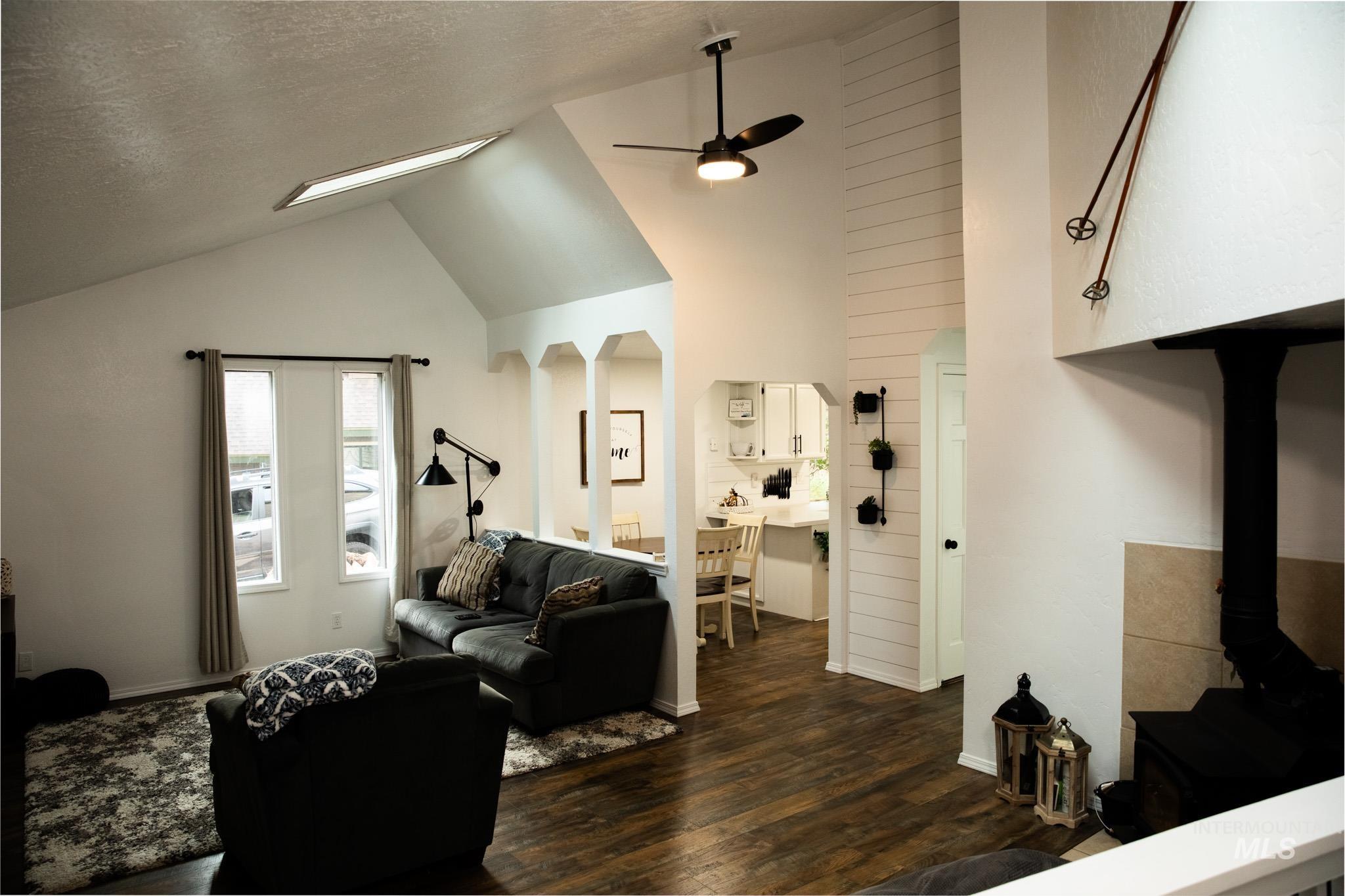Living room with dark wood-style floors, arched walkways, high vaulted ceiling, a textured ceiling, and a wood stove