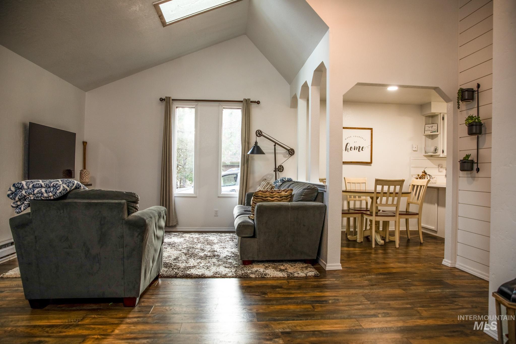 Living area featuring vaulted ceiling, dark wood-style flooring, a skylight, and arched walkways
