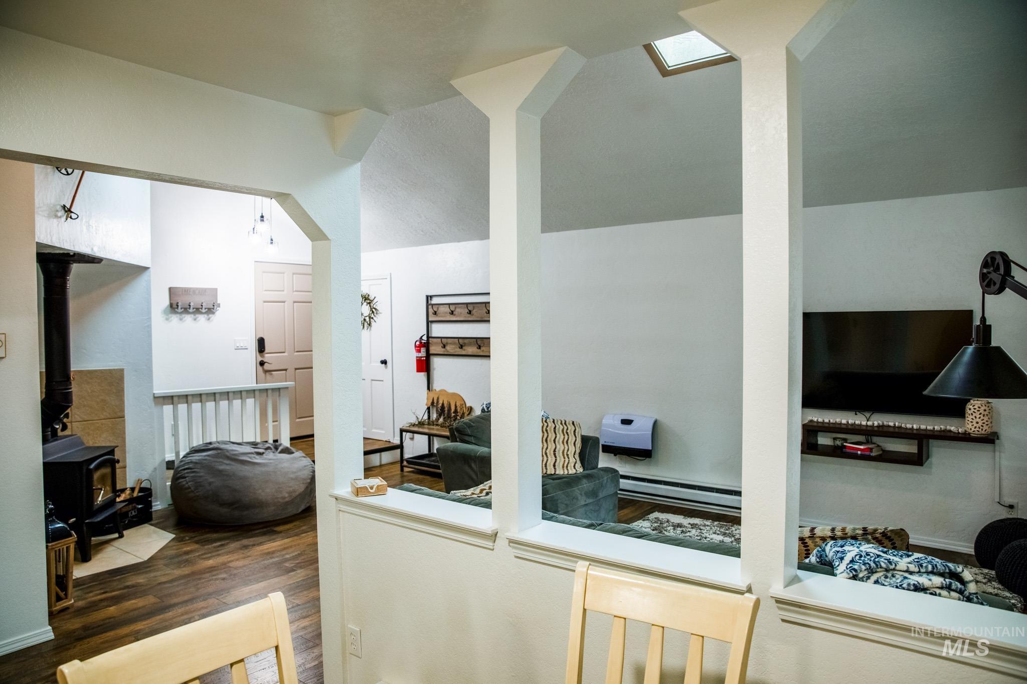 Kitchen featuring a wood stove, arched walkways, lofted ceiling, wood finished floors, and baseboard heating