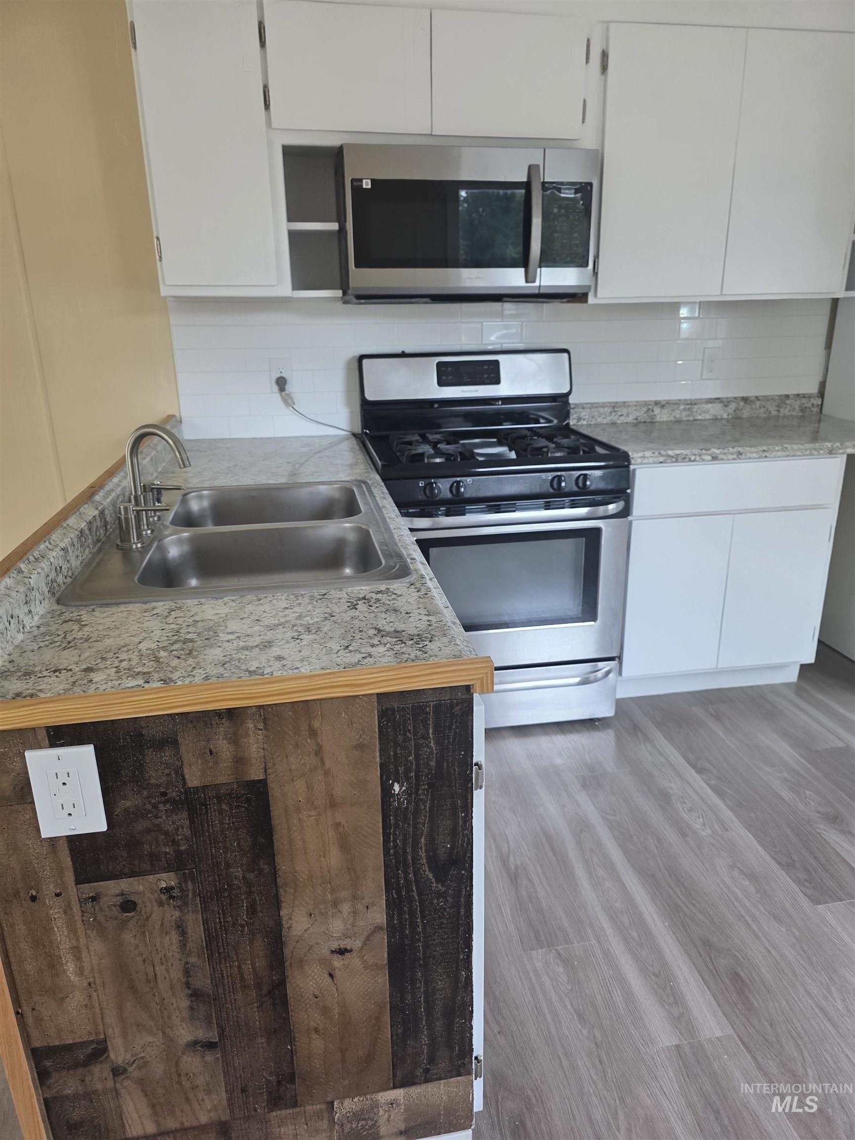 Kitchen with appliances with stainless steel finishes, light countertops, tasteful backsplash, light wood finished floors, and white cabinetry