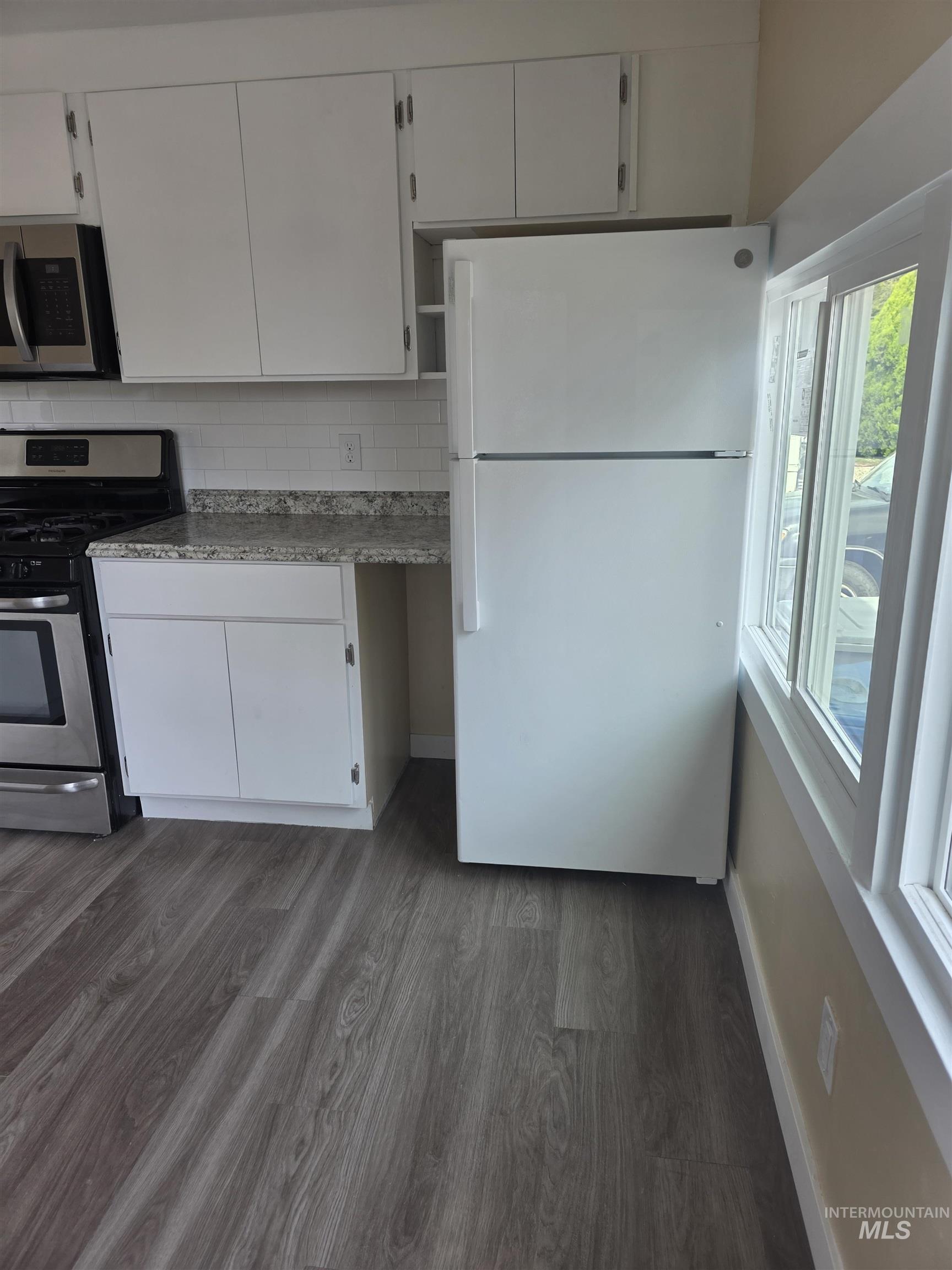 Kitchen featuring appliances with stainless steel finishes, white cabinets, dark wood-style flooring, and decorative backsplash