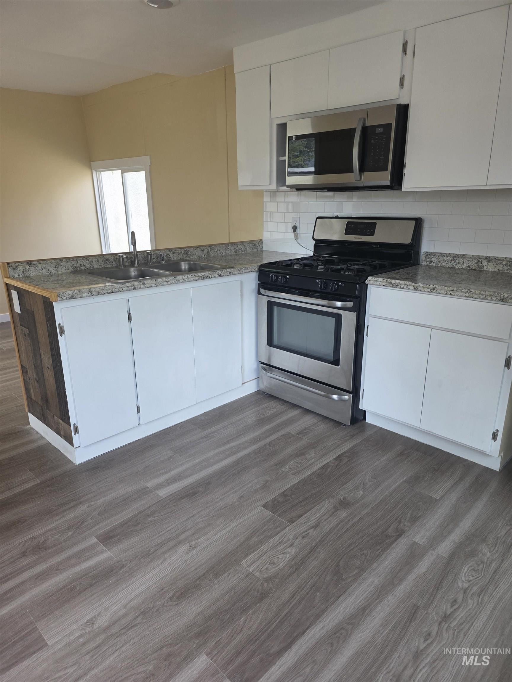 Kitchen with appliances with stainless steel finishes, white cabinetry, dark wood finished floors, and tasteful backsplash