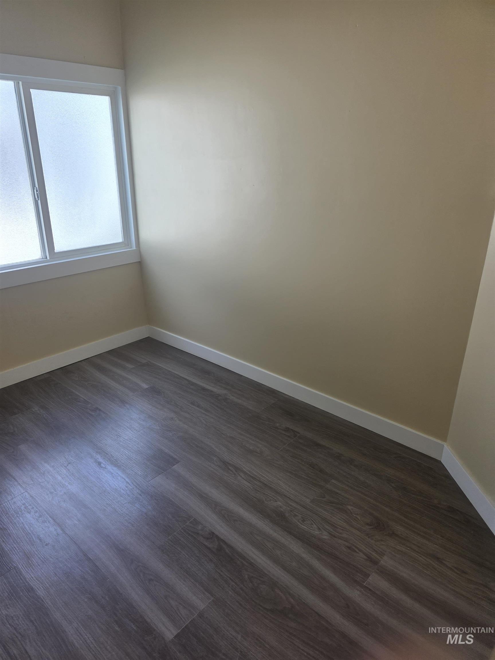 Empty room featuring baseboards and dark wood-style flooring