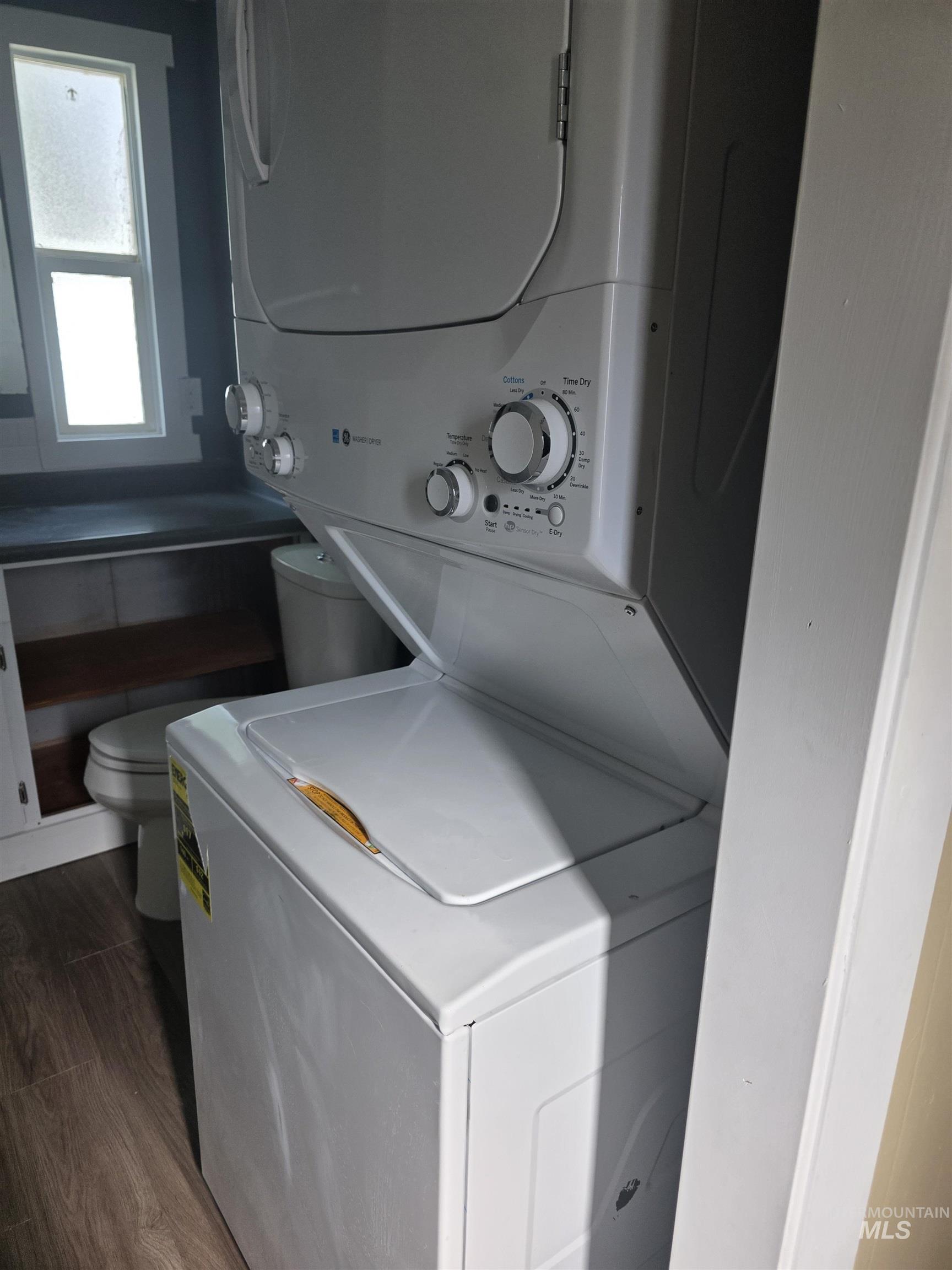 Washroom with estacked washer and dryer and dark wood-type flooring