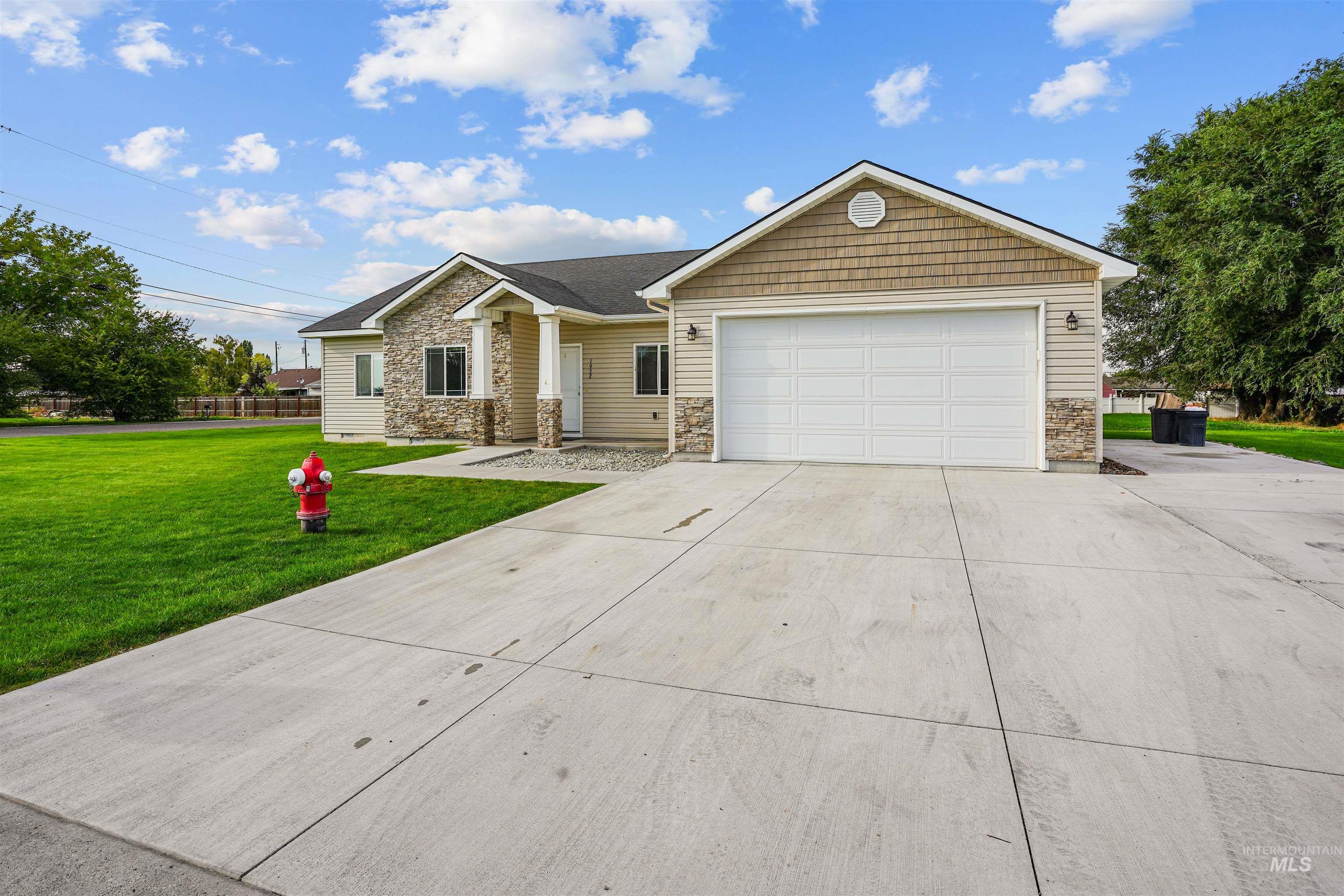 View of front facade with a front yard, driveway, stone siding, and a garage