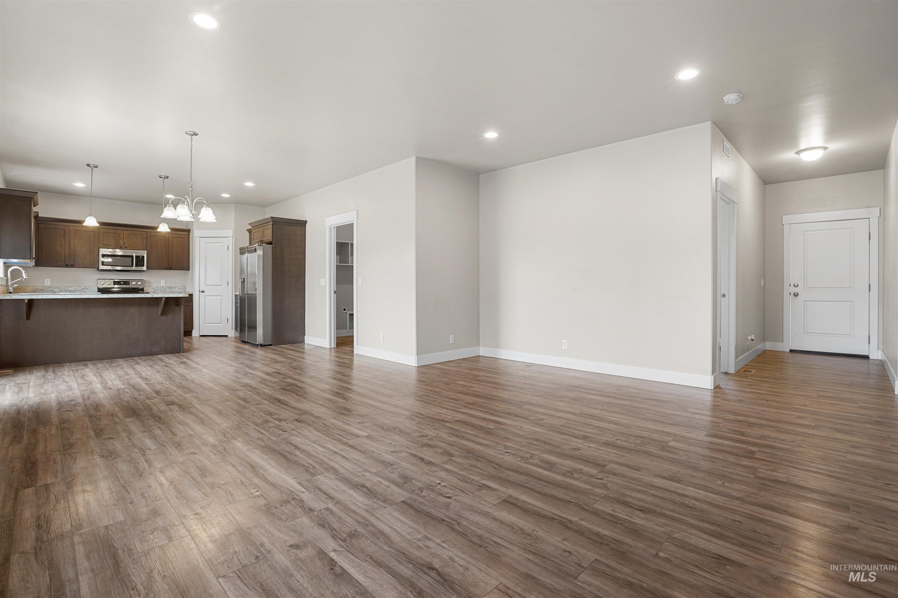 Unfurnished living room featuring dark wood-style flooring, recessed lighting, and a chandelier