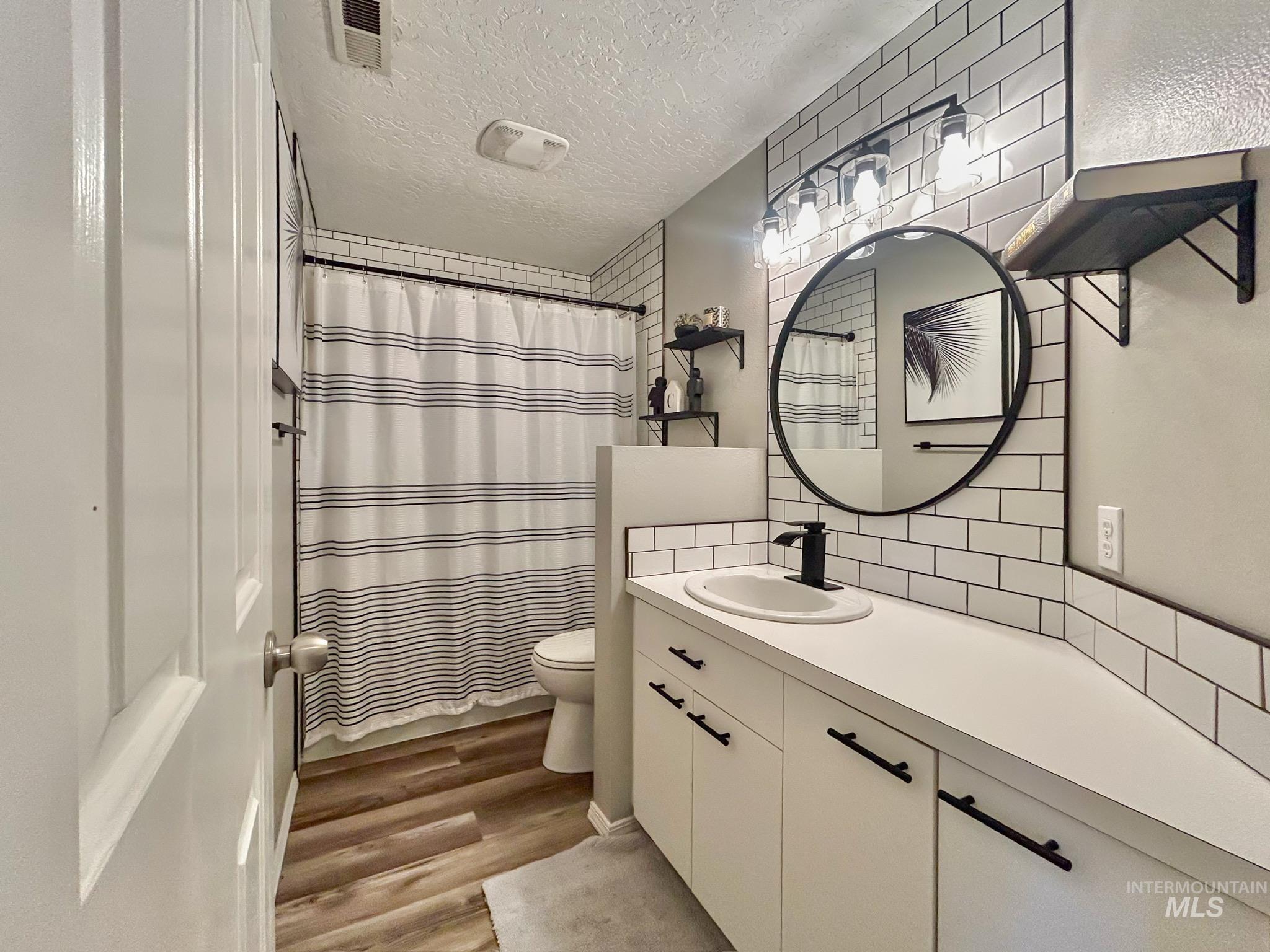 Full bath featuring vanity, a textured ceiling, dark wood finished floors, backsplash, and curtained shower