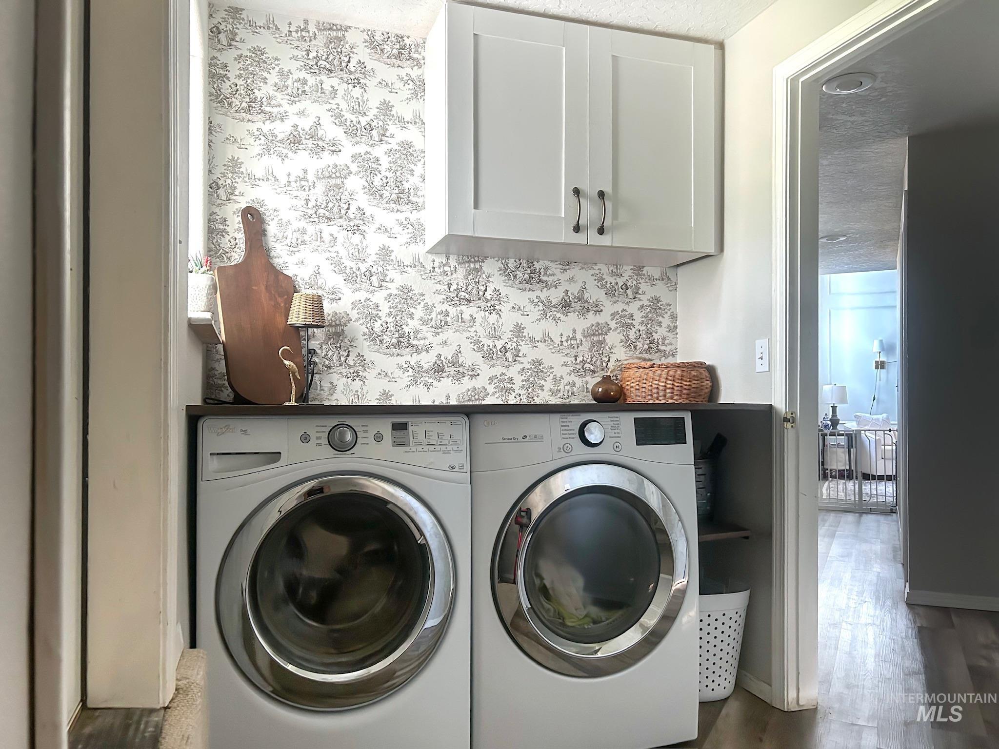 Laundry room featuring wallpapered walls, cabinet space, wood finished floors, and washing machine and clothes dryer