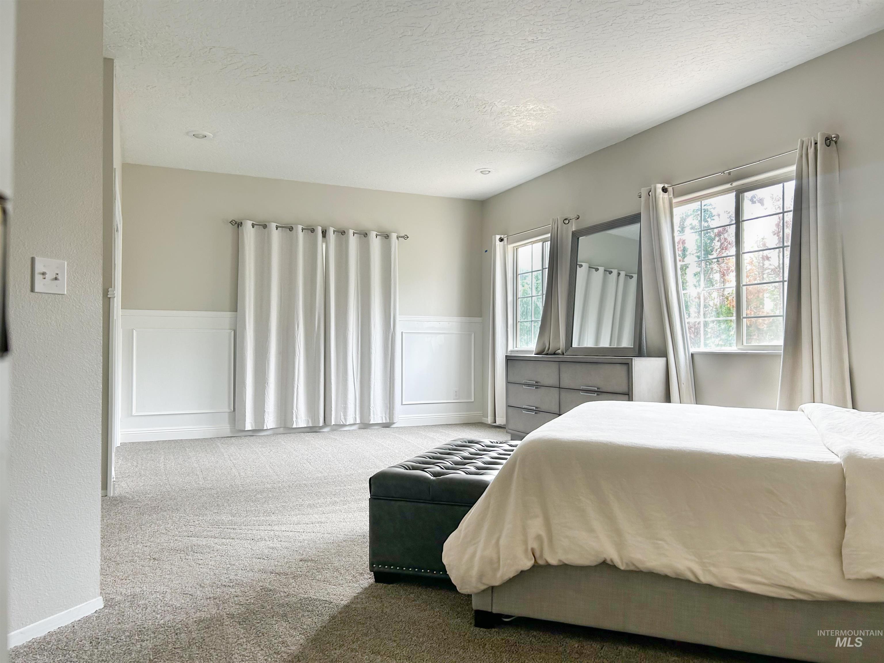 Bedroom with carpet, a decorative wall, a textured ceiling, and wainscoting
