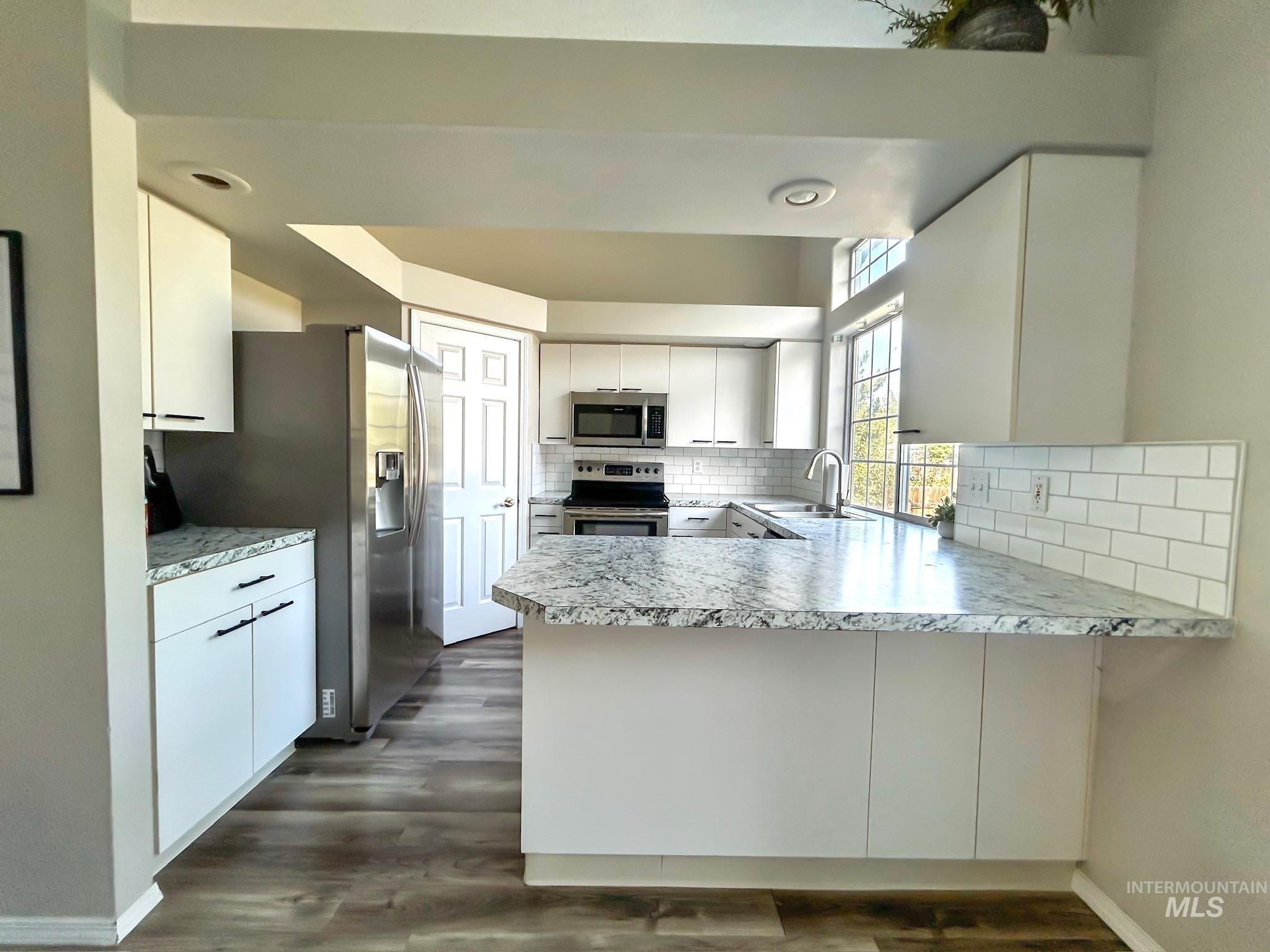 Kitchen with a peninsula, light countertops, appliances with stainless steel finishes, and white cabinets