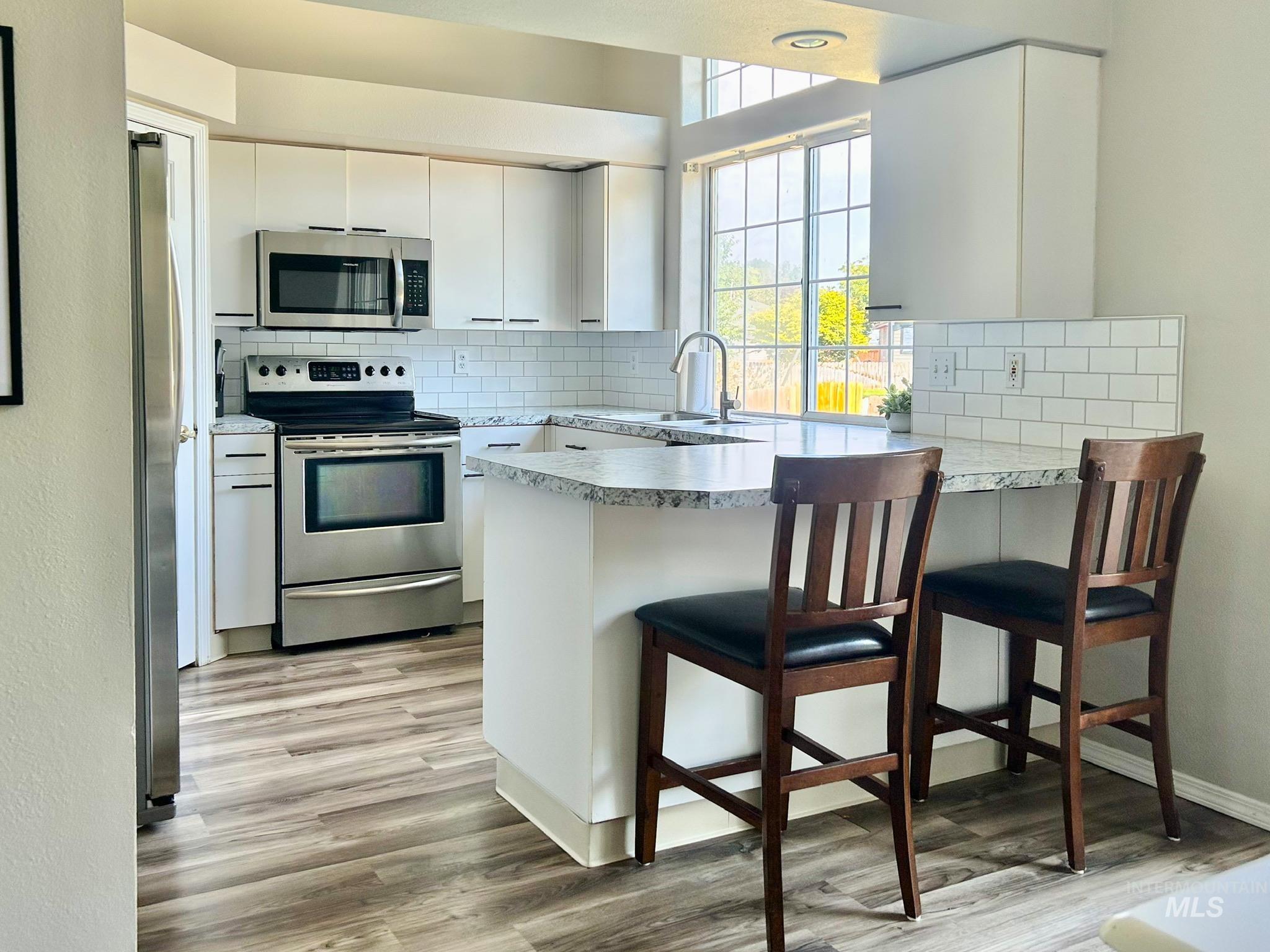 Kitchen featuring appliances with stainless steel finishes, light countertops, white cabinetry, and a kitchen bar