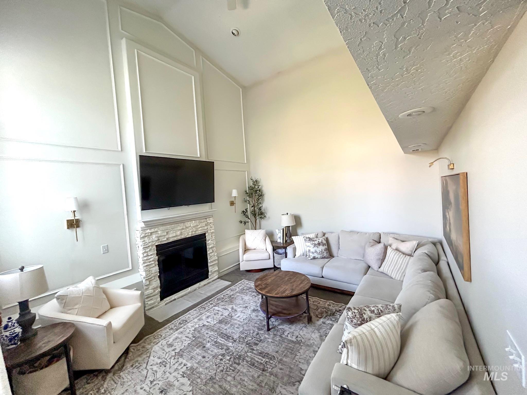 Living room featuring a stone fireplace, a textured ceiling, and vaulted ceiling