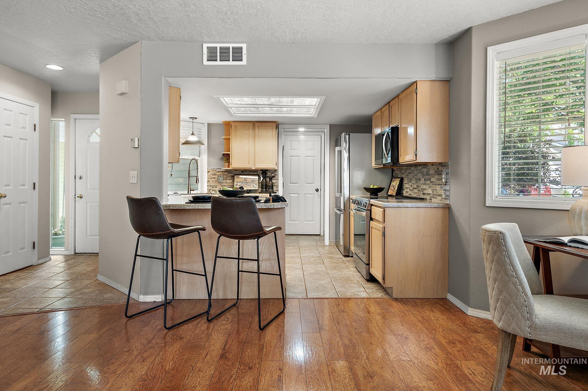 Kitchen with stainless steel appliances, a breakfast bar, a peninsula, decorative backsplash, and light wood-style flooring