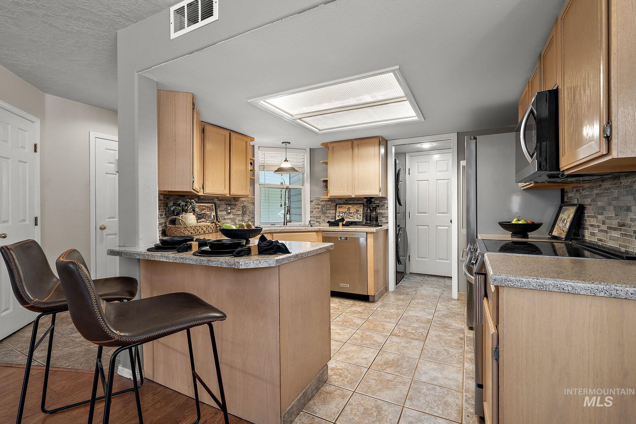 Kitchen with appliances with stainless steel finishes, a peninsula, backsplash, and a breakfast bar area
