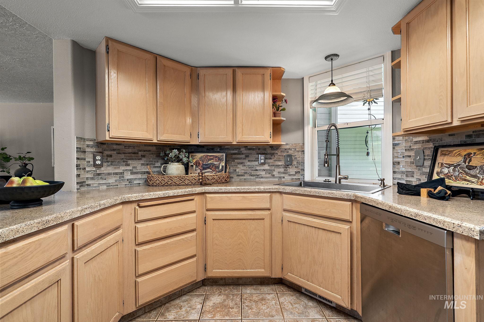 Kitchen with stainless steel dishwasher, open shelves, light brown cabinets, and light countertops