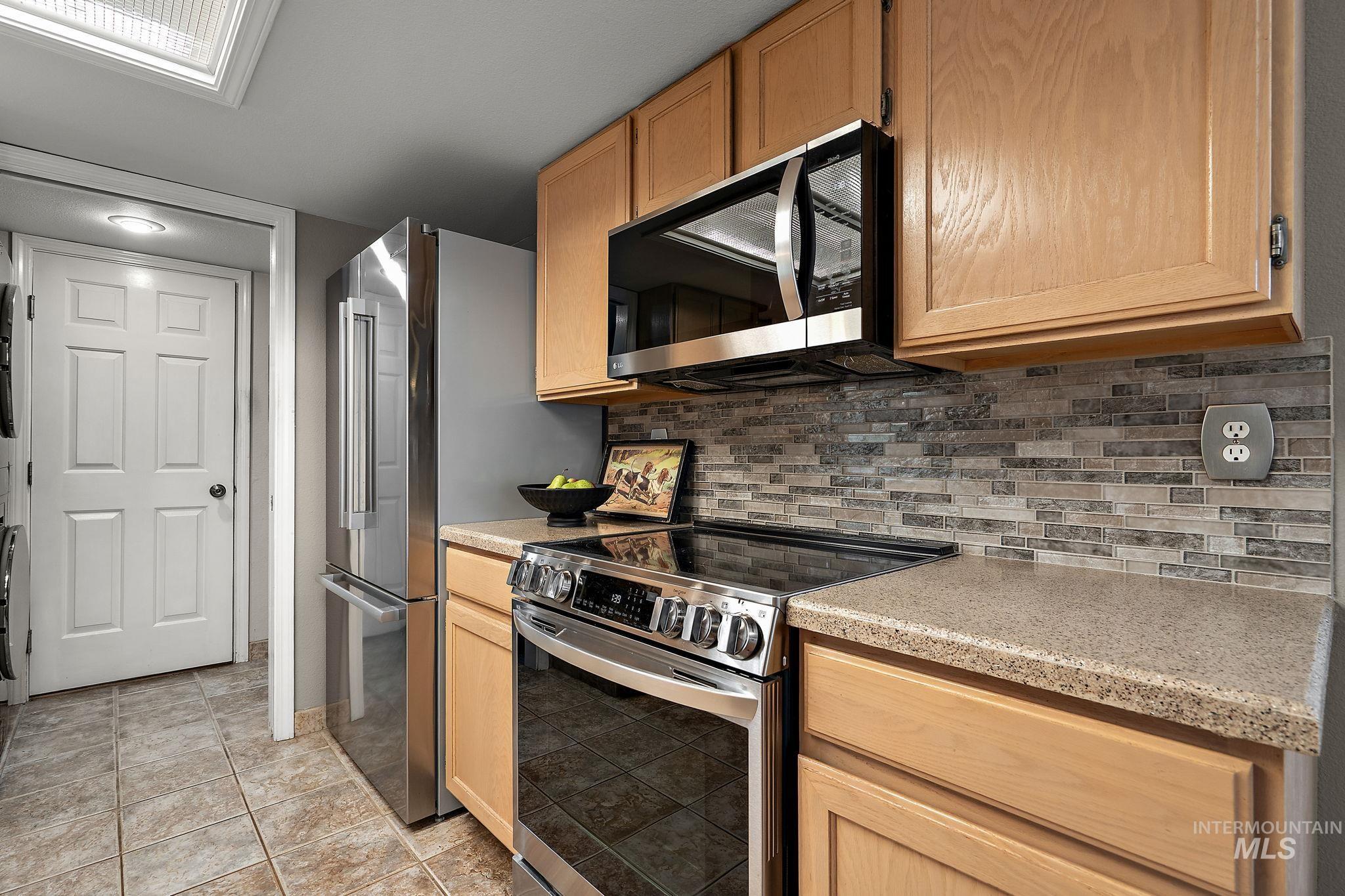 Kitchen with appliances with stainless steel finishes, backsplash, light countertops, and light brown cabinets