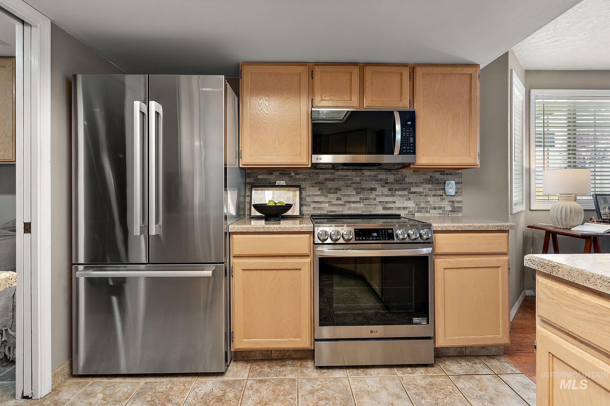 Kitchen featuring stainless steel appliances, light countertops, backsplash, and light brown cabinets