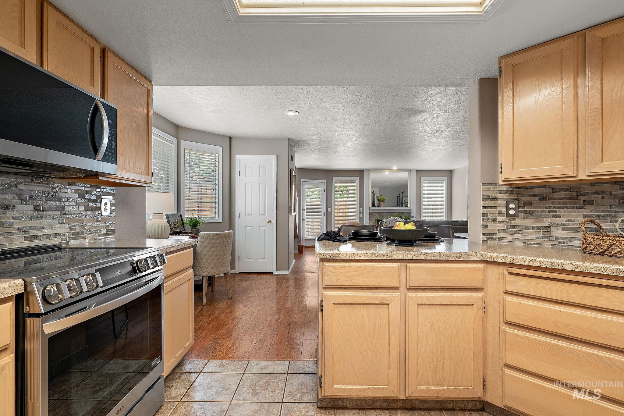 Kitchen featuring appliances with stainless steel finishes, a peninsula, tasteful backsplash, light countertops, and open floor plan
