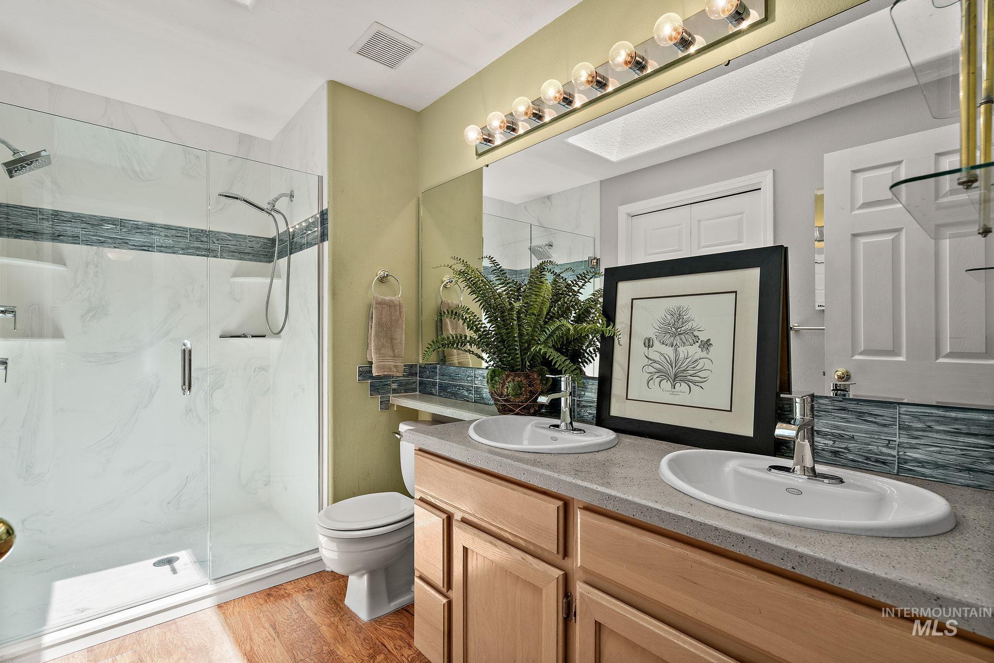 Full bath featuring a marble finish shower, double vanity, and wood finished floors