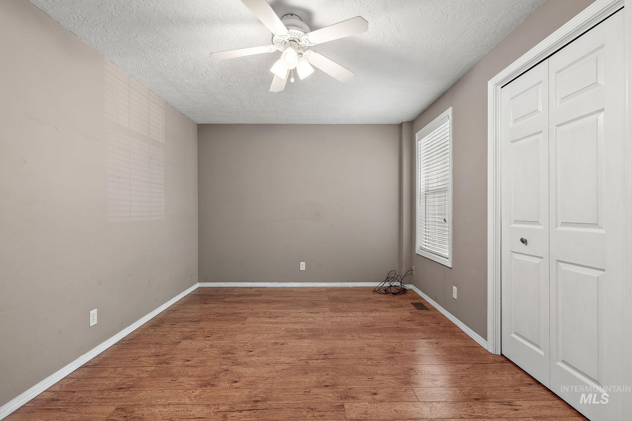 Unfurnished bedroom with a textured ceiling, wood finished floors, a closet, and ceiling fan