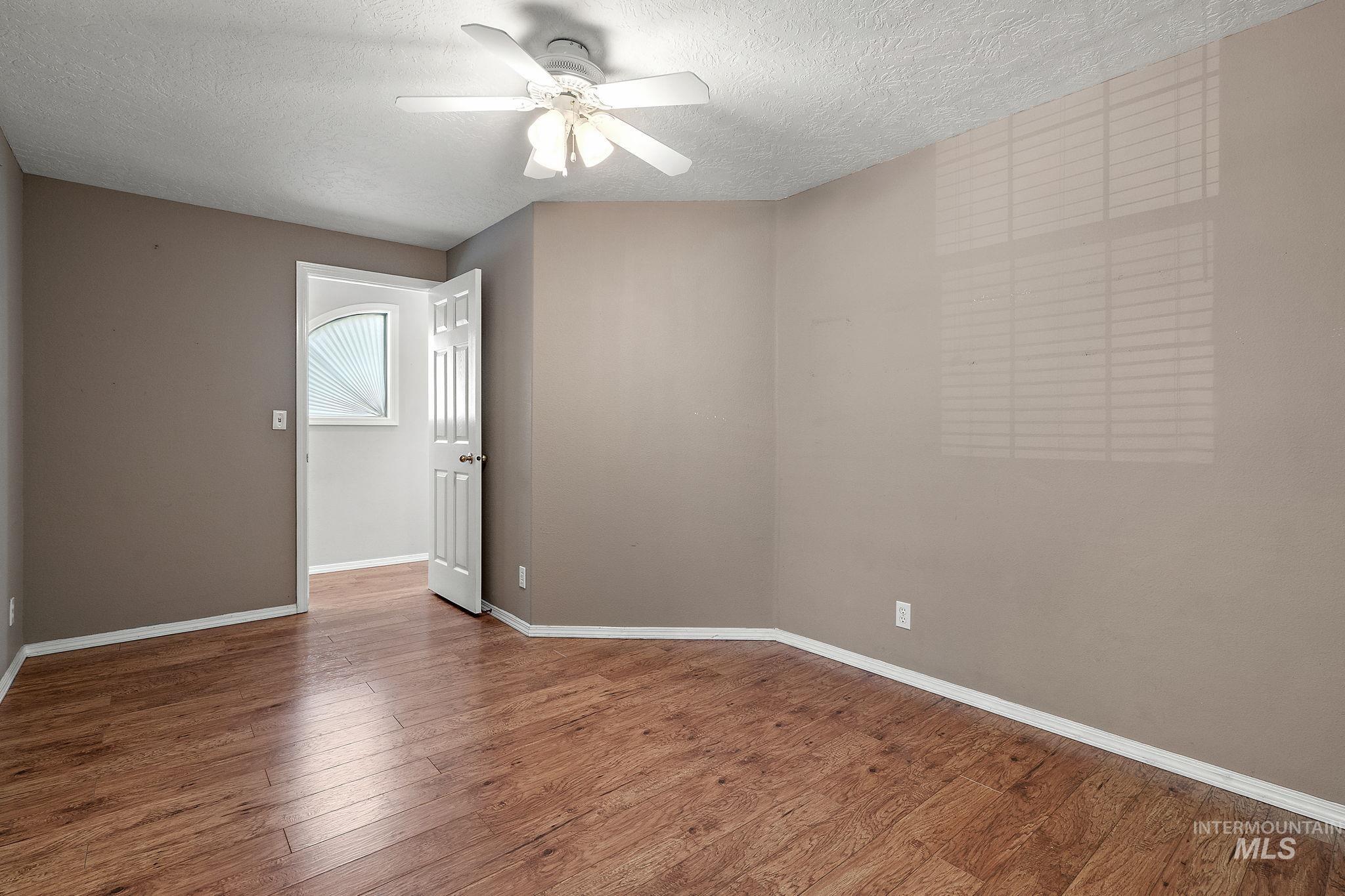 Empty room with ceiling fan, a textured ceiling, and wood finished floors