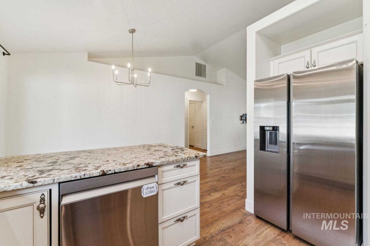Kitchen with appliances with stainless steel finishes, lofted ceiling, light wood-style floors, arched walkways, and light stone counters