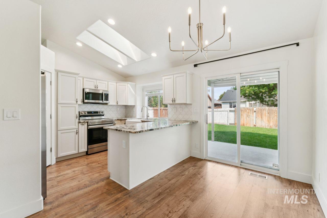 Kitchen with tasteful backsplash, stainless steel appliances, light stone countertops, white cabinets, and lofted ceiling