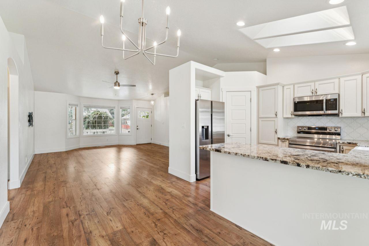 Kitchen with light stone counters, backsplash, stainless steel appliances, light wood-type flooring, and lofted ceiling