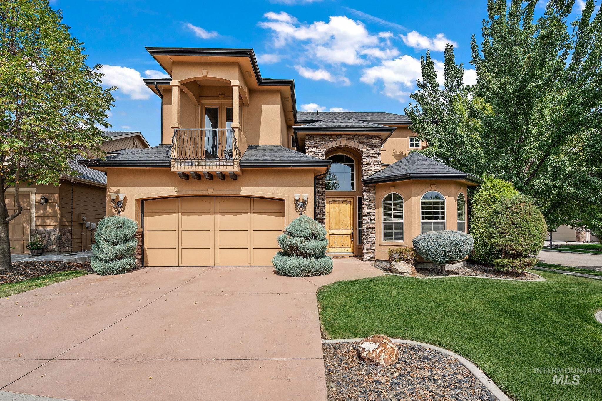 View of front of house featuring stone siding, stucco siding, a front yard, concrete driveway, and a balcony