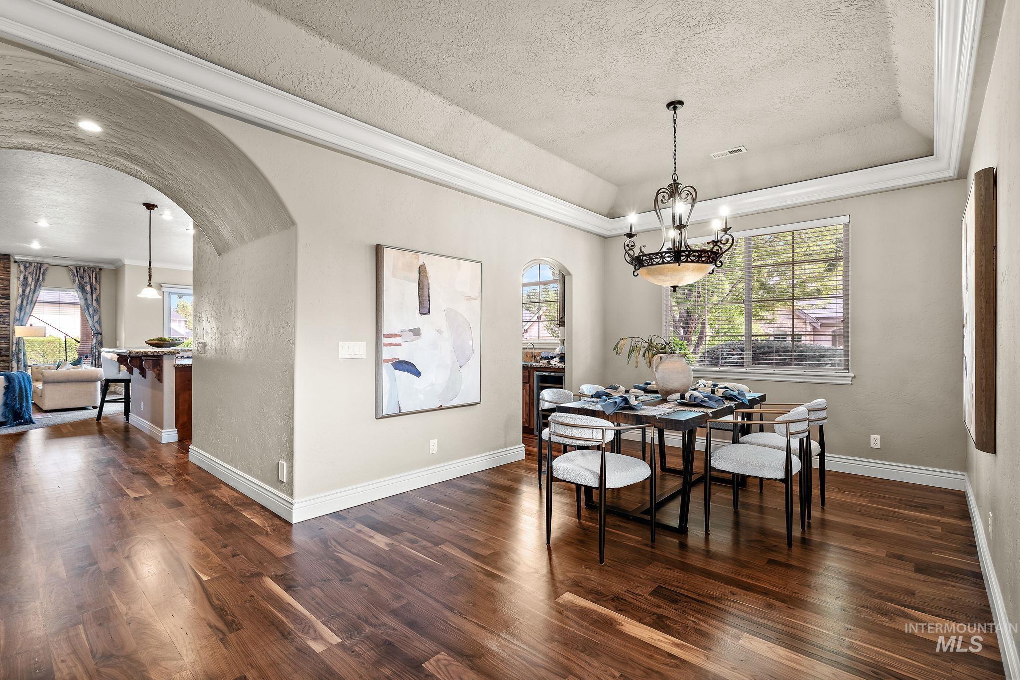 Dining room featuring arched walkways, ornamental molding, a textured ceiling, healthy amount of natural light, and dark wood finished floors