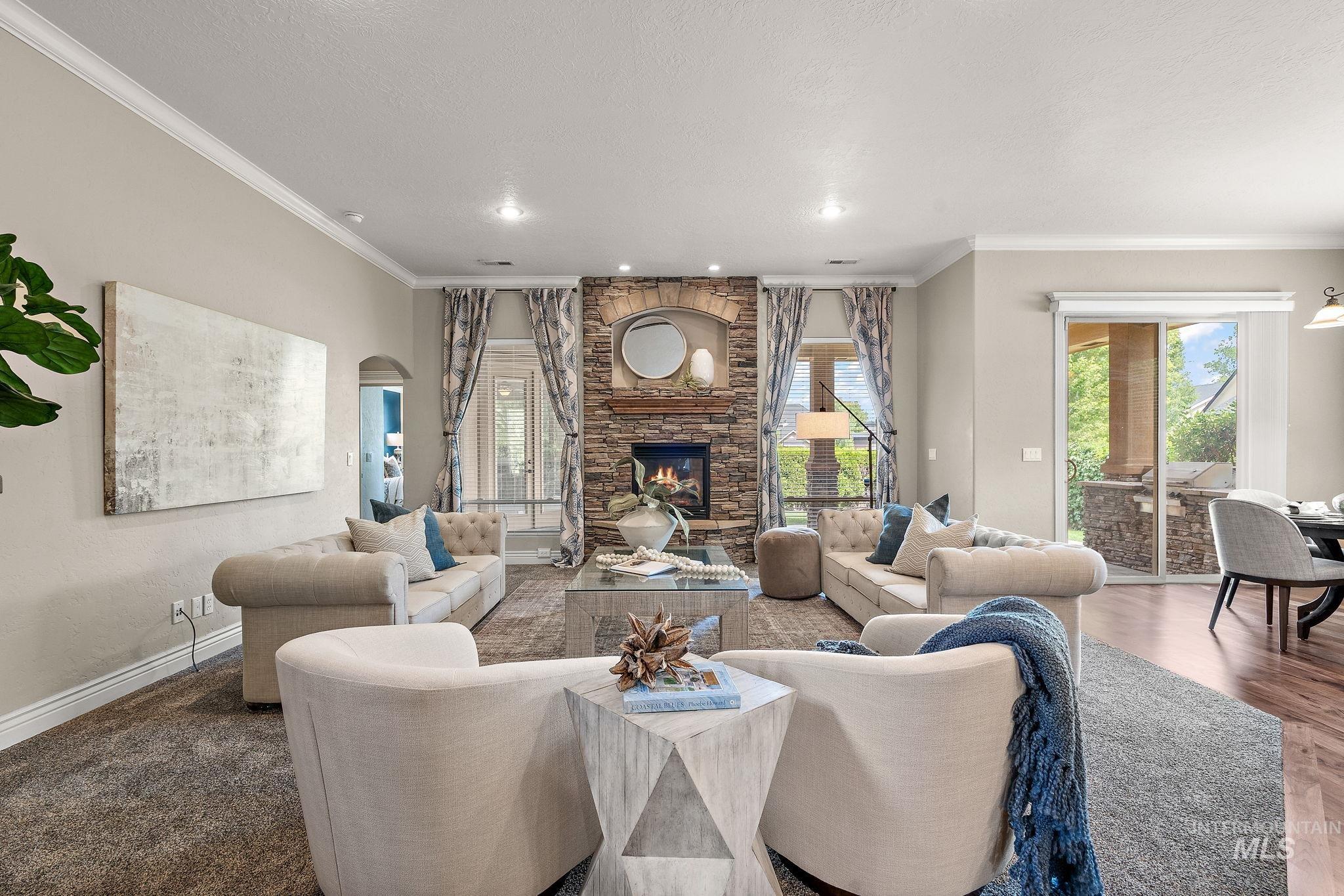 Living room featuring crown molding, a stone fireplace, arched walkways, recessed lighting, and a textured ceiling