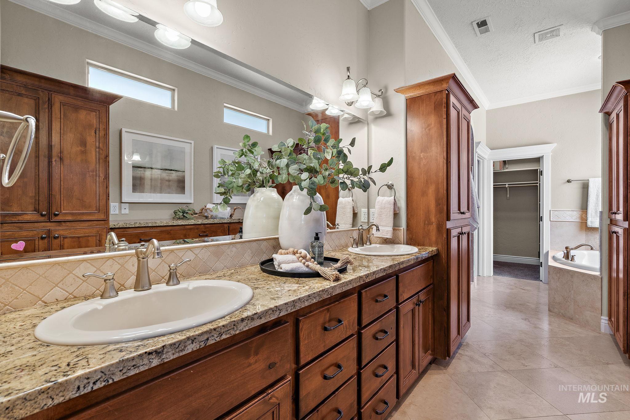Bathroom featuring ornamental molding, double vanity, a garden tub, light tile patterned floors, and a walk in closet