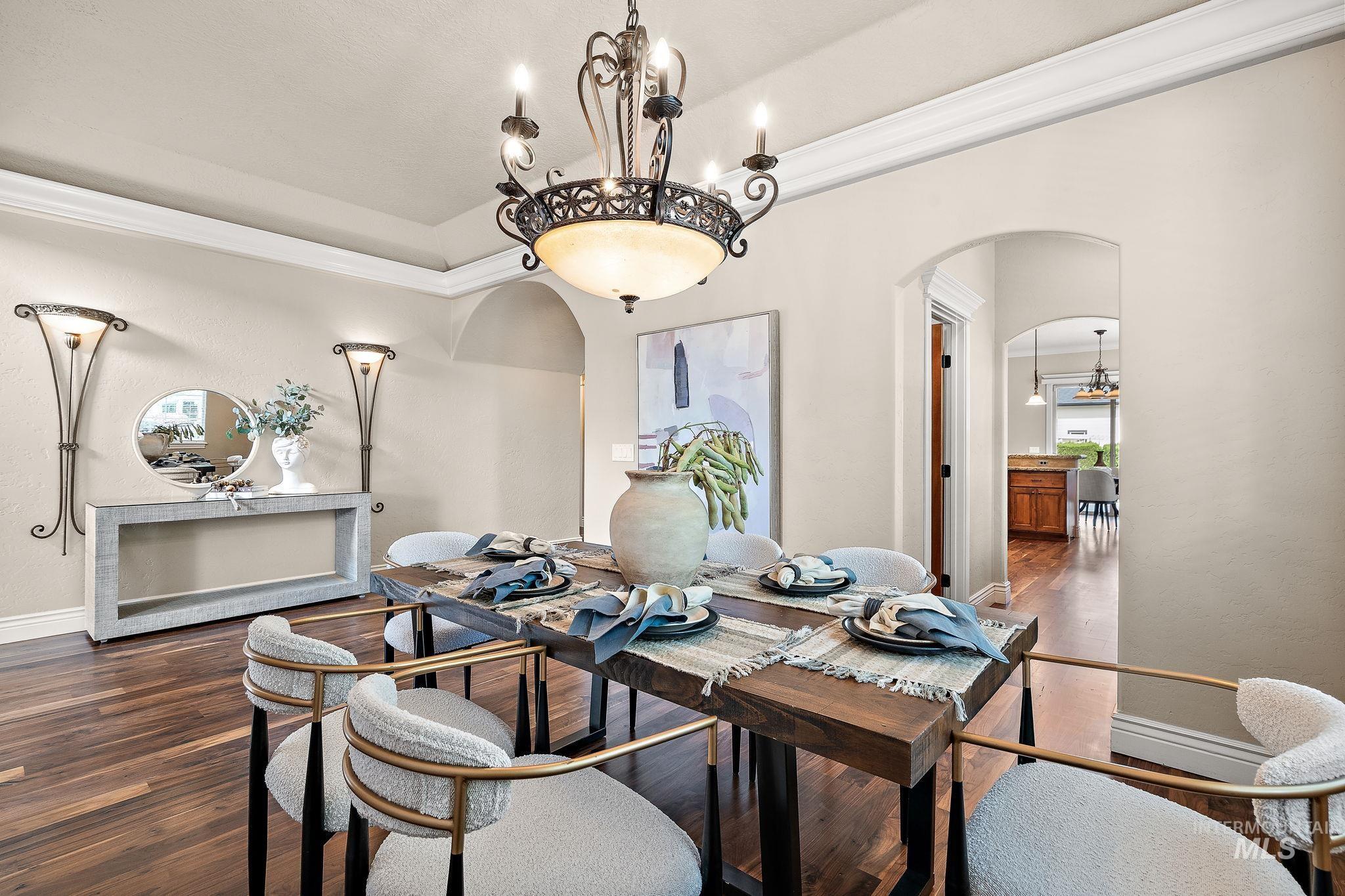 Dining area with a chandelier, crown molding, dark wood-type flooring, arched walkways, and a raised ceiling