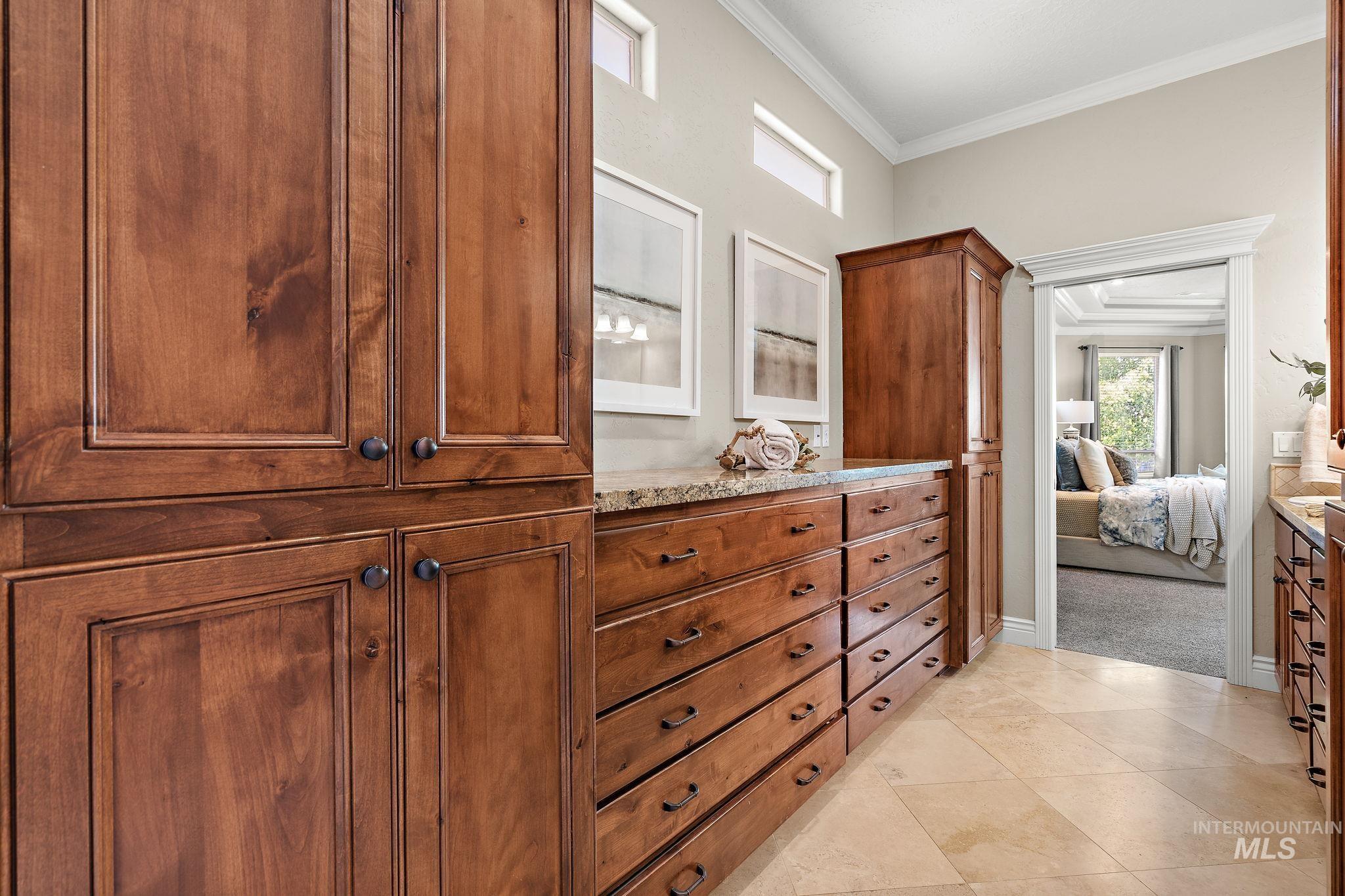 Ensuite bathroom featuring vanity, crown molding, and light tile patterned floors