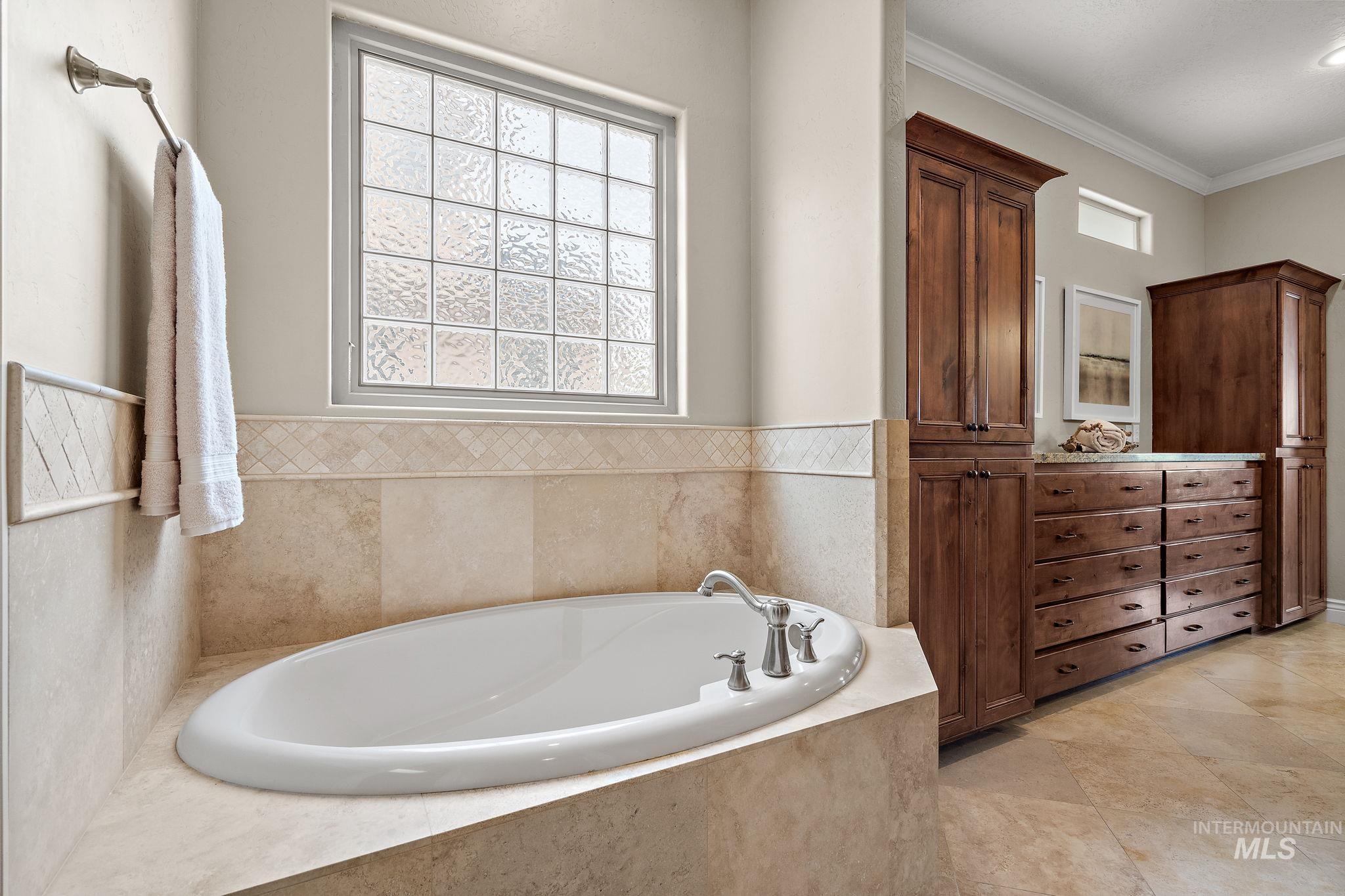 Full bathroom featuring a garden tub, crown molding, vanity, and light tile patterned floors