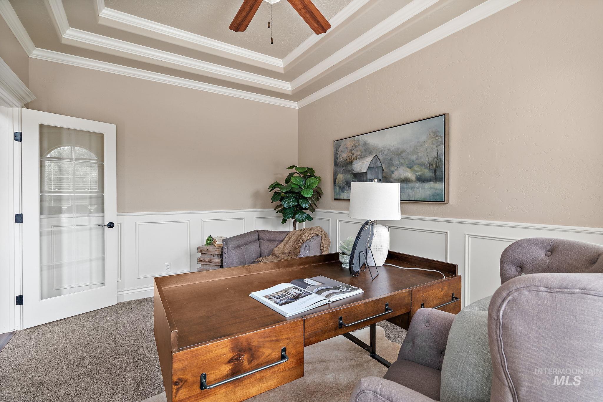 Office area with a tray ceiling, a decorative wall, carpet, wainscoting, and ornamental molding
