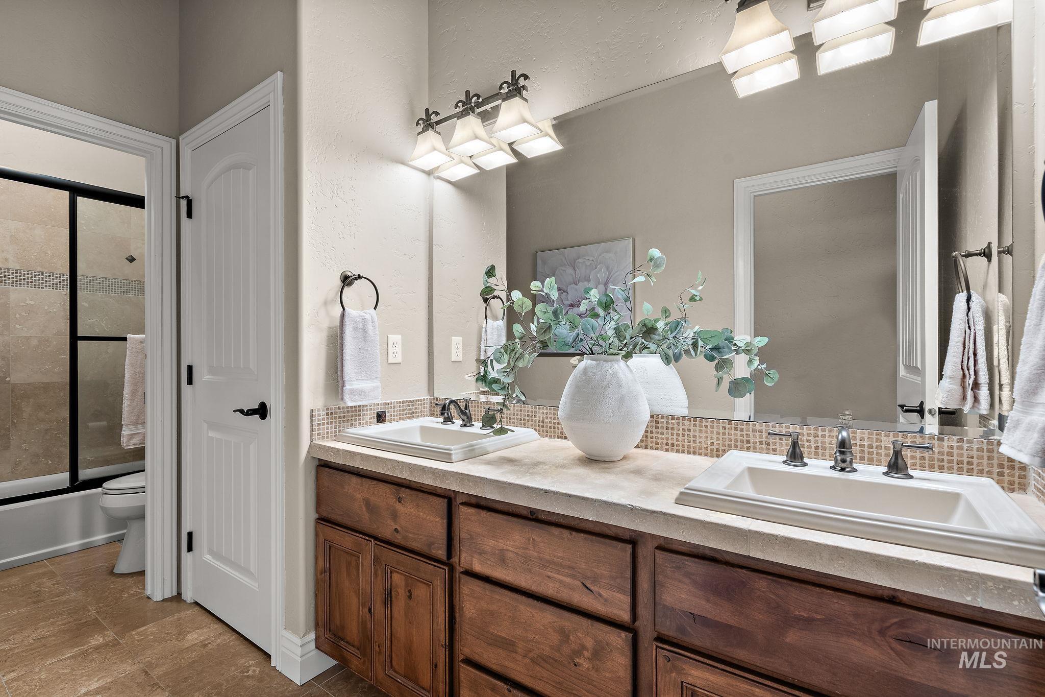 Full bathroom with double vanity, shower / bath combination with glass door, and a textured wall