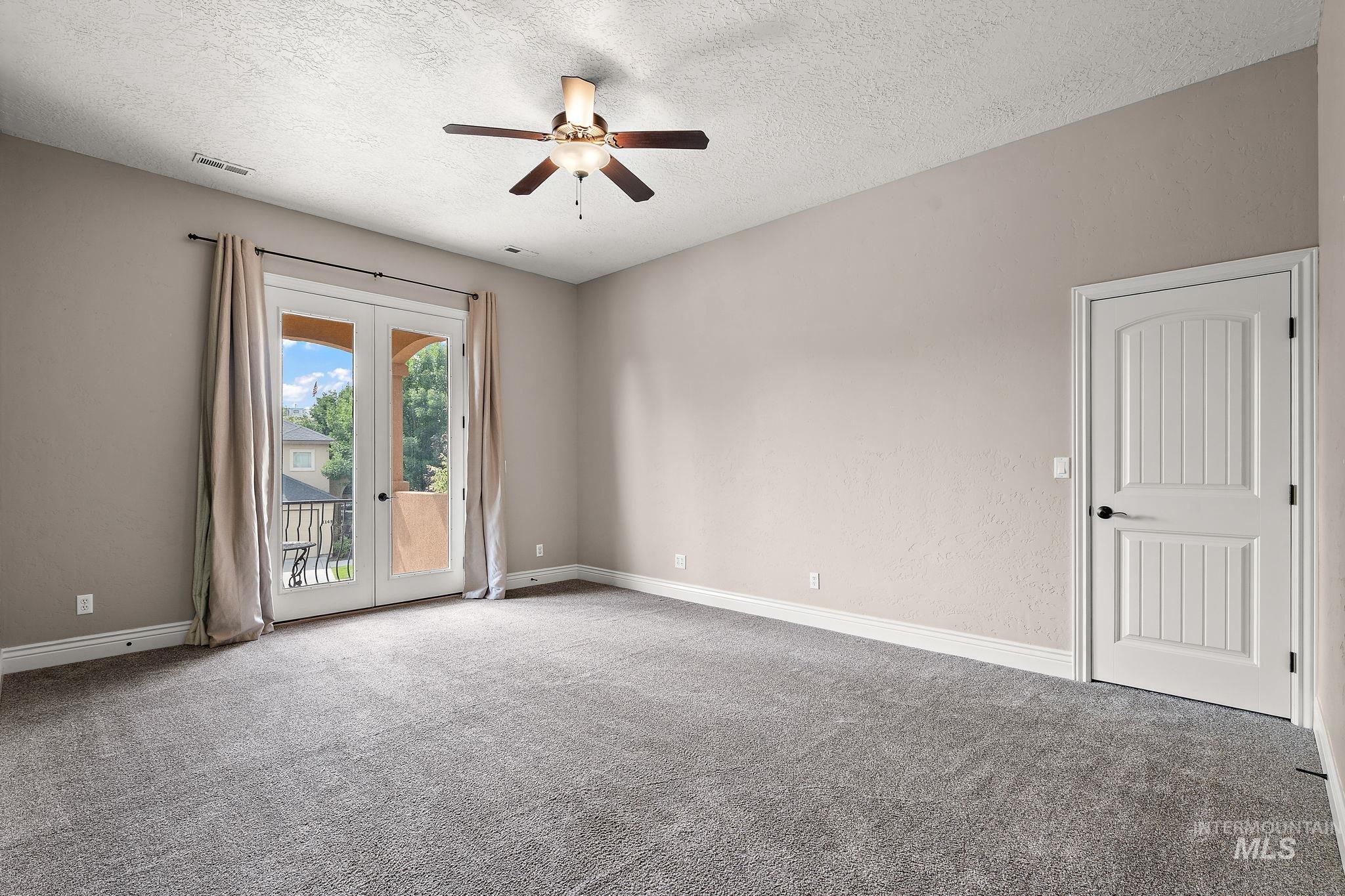 Carpeted empty room featuring french doors, a textured ceiling, and ceiling fan