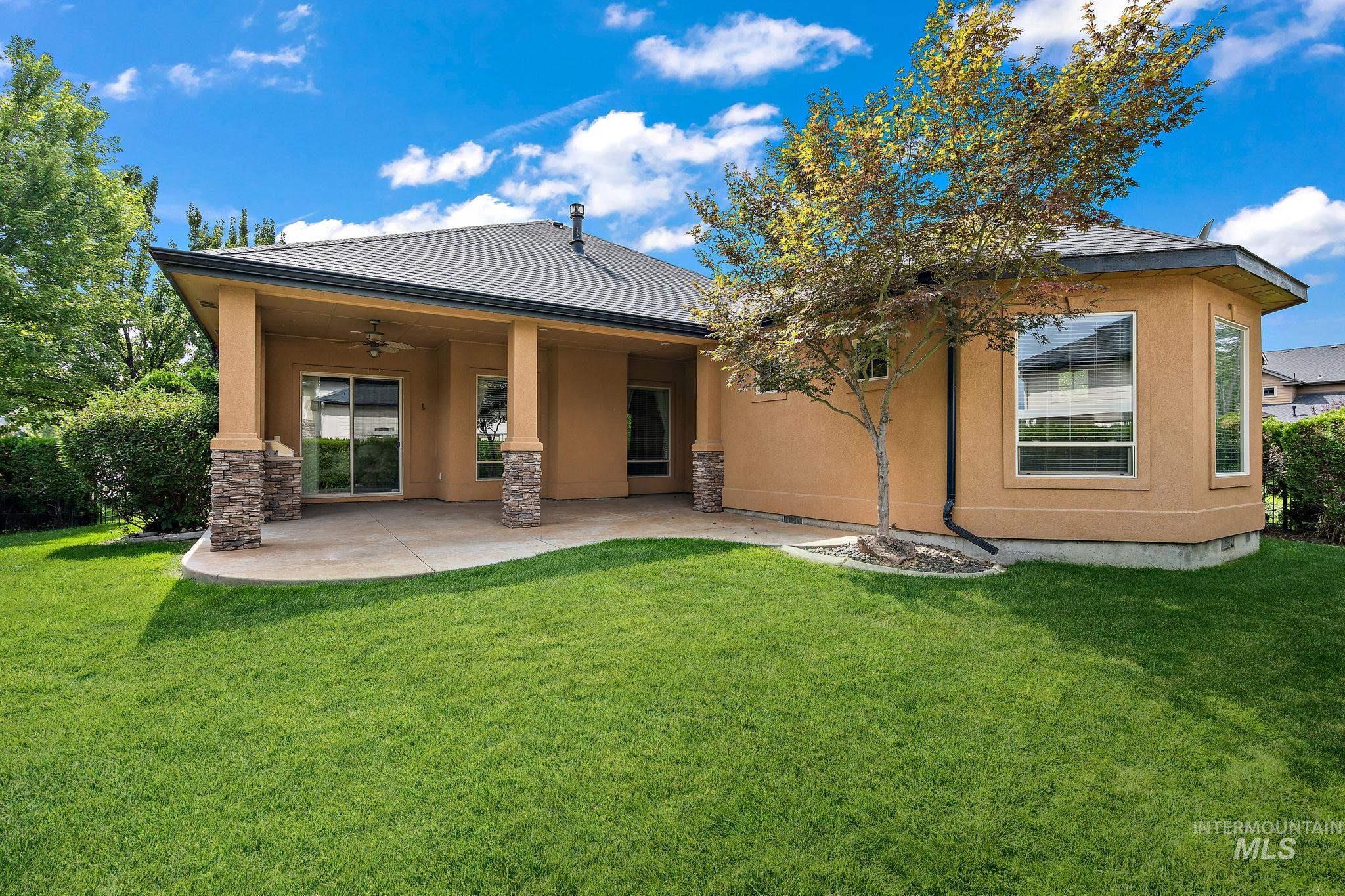 Rear view of house with stucco siding, roof with shingles, a patio area, a lawn, and a ceiling fan