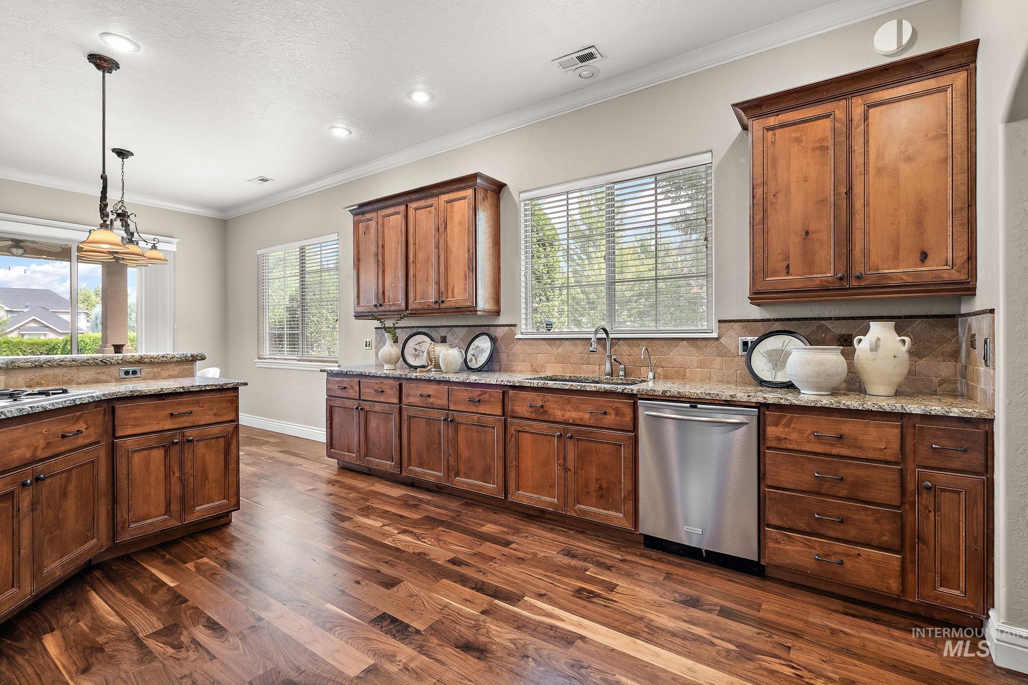 Kitchen featuring tasteful backsplash, crown molding, light stone countertops, stainless steel dishwasher, and decorative light fixtures
