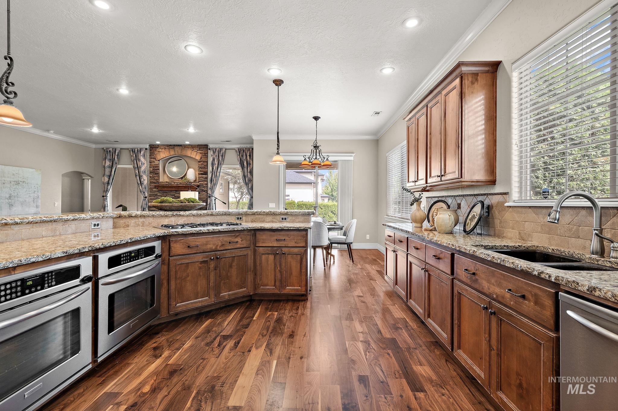Kitchen with crown molding, appliances with stainless steel finishes, pendant lighting, light stone counters, and arched walkways
