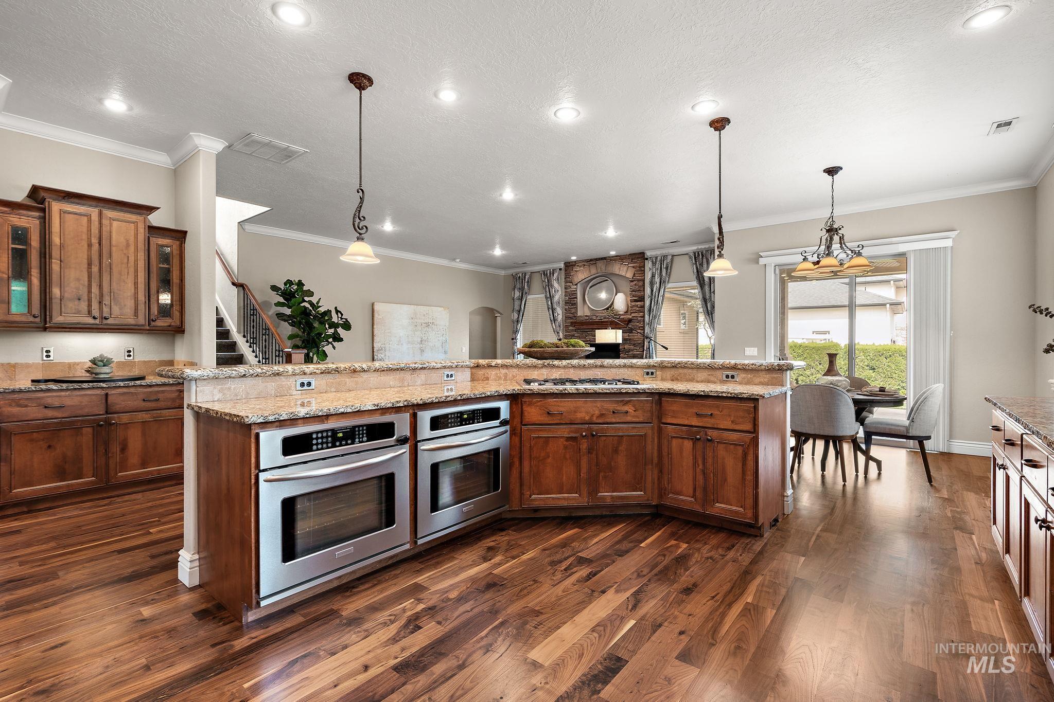 Kitchen with glass insert cabinets, crown molding, decorative light fixtures, brown cabinets, and light stone countertops