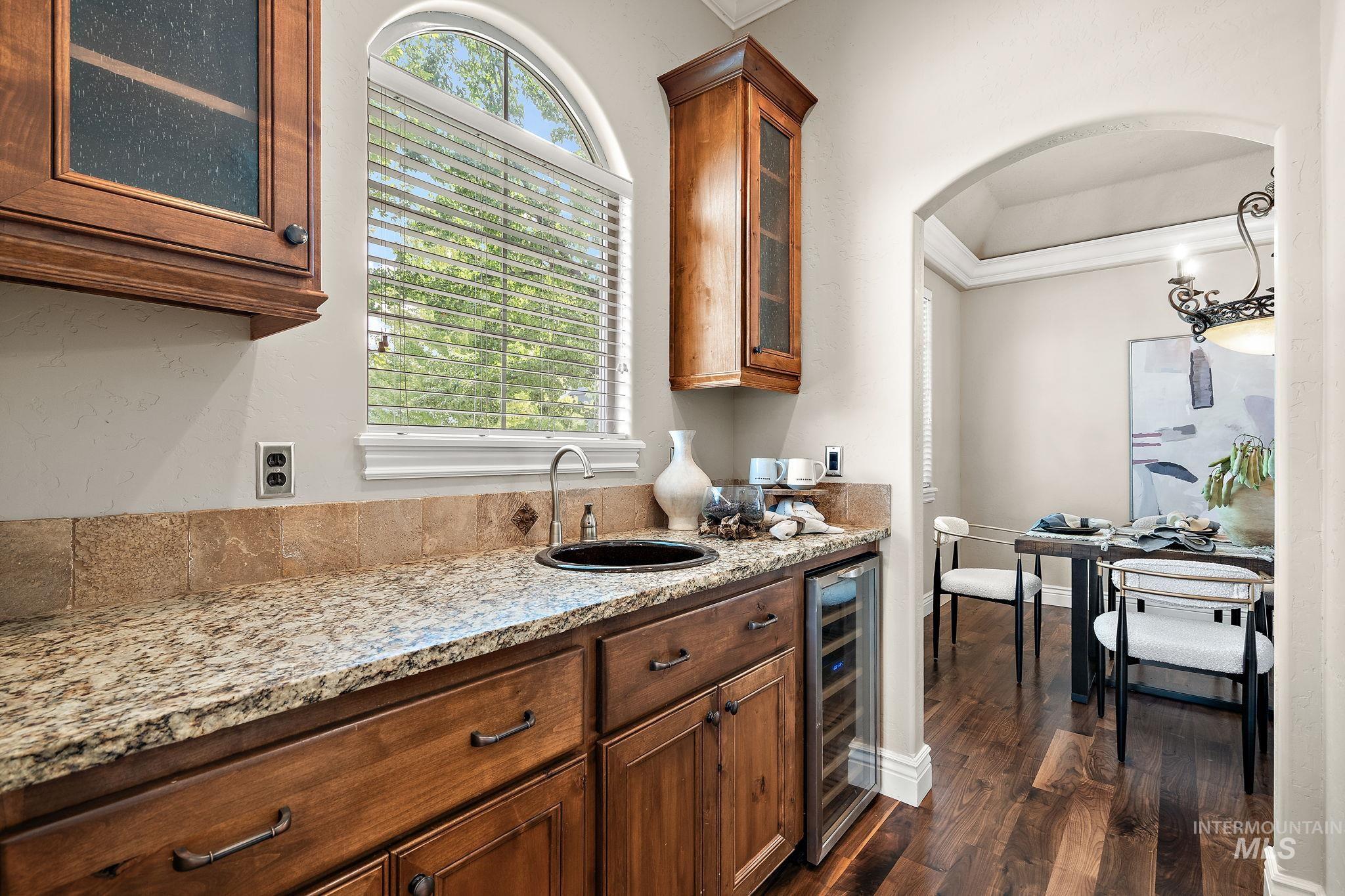 Kitchen with glass insert cabinets, light stone countertops, dark wood-type flooring, brown cabinets, and beverage cooler