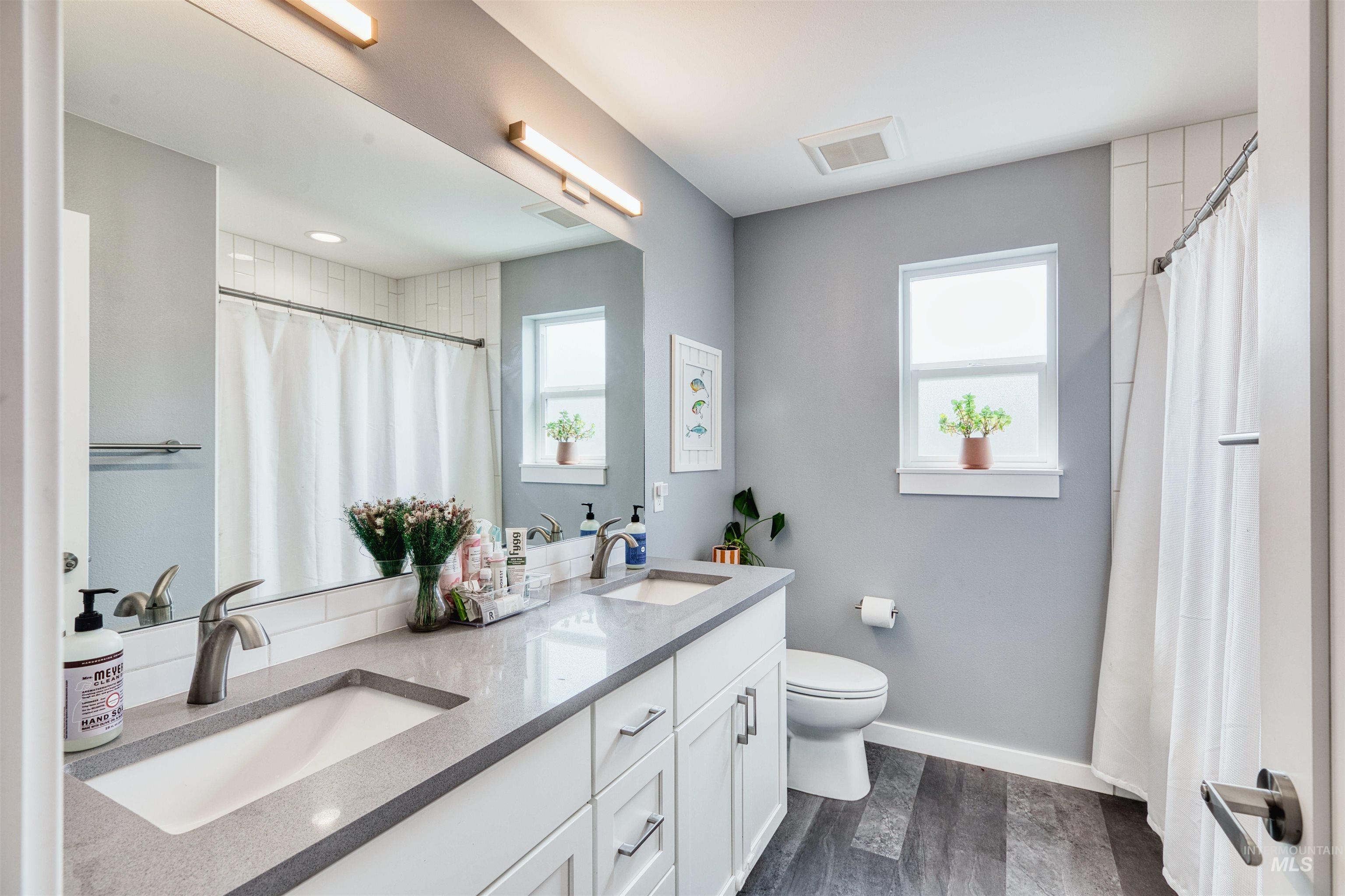 Bathroom with double vanity, dark wood finished floors, and curtained shower