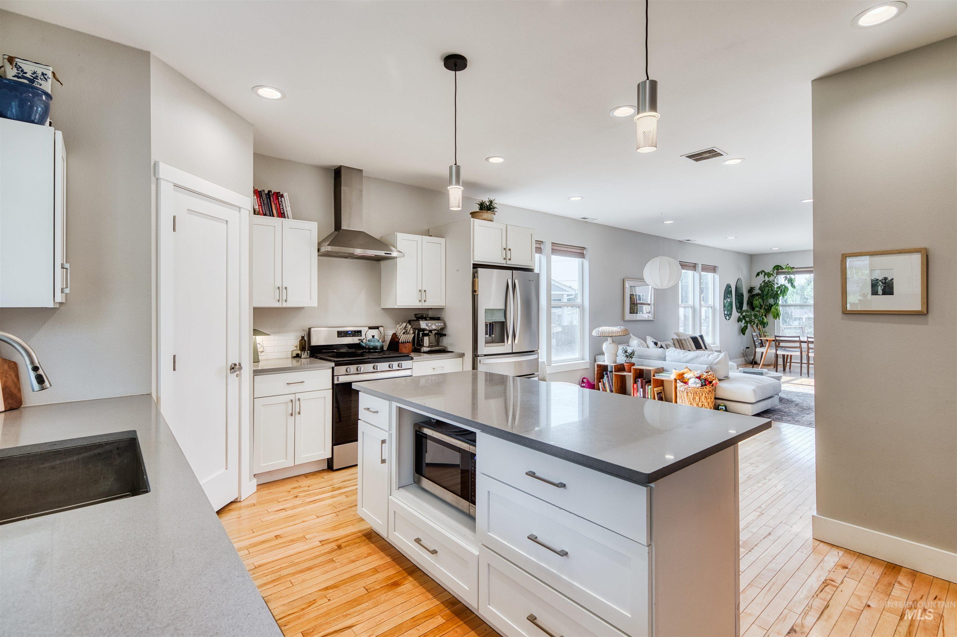 Kitchen featuring hanging light fixtures, appliances with stainless steel finishes, wall chimney exhaust hood, a center island, and light wood-type flooring